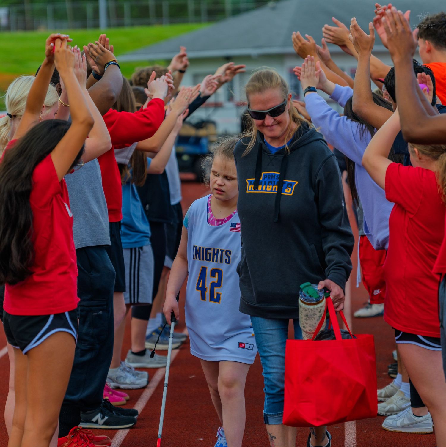 Young girl in Knights #42 jersey walks through a celebratory tunnel of raised hands on a track.