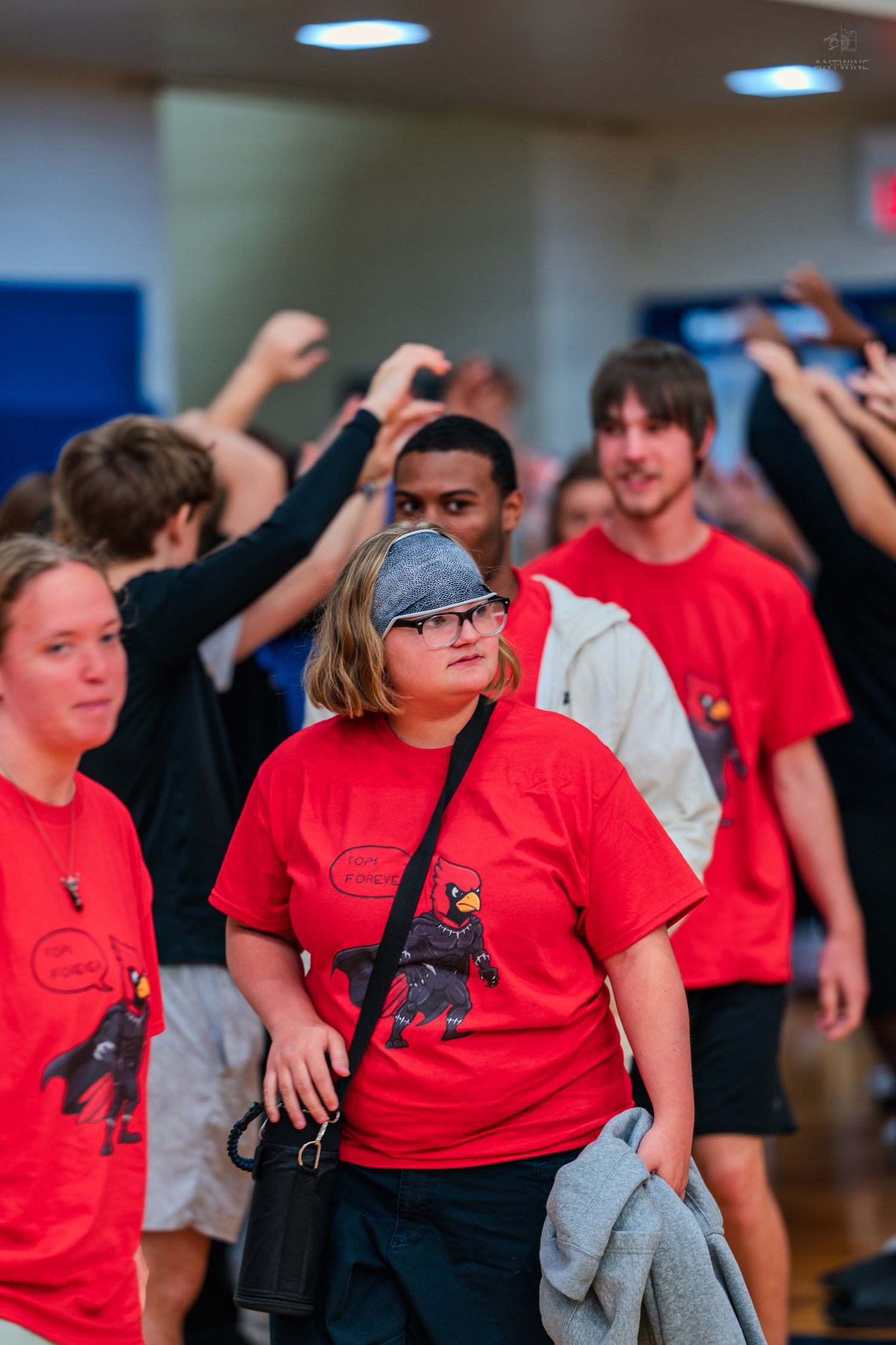 Students in red Cardinal t-shirts walk through a gymnasium during a school orientation or pep rally event.