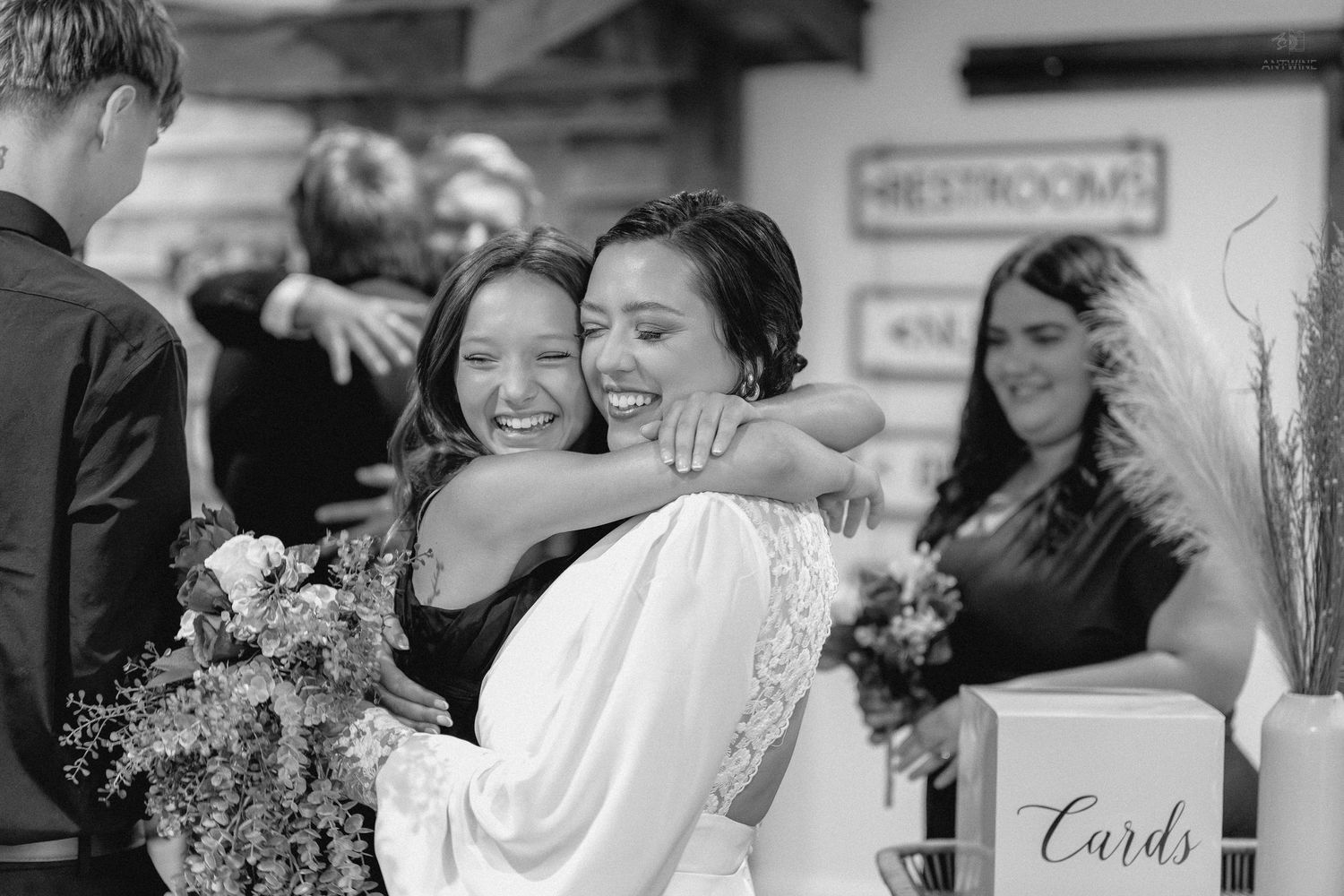 Bride joyfully embraces a guest in a warm hug at her wedding reception celebration.