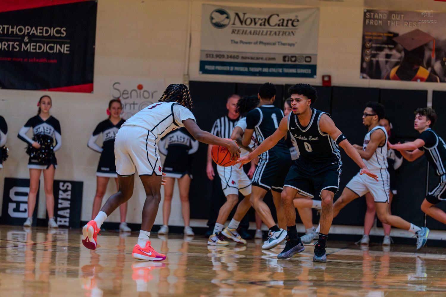 High school basketball players compete on the court during an intense game with NovaCare sponsorship banners visible.