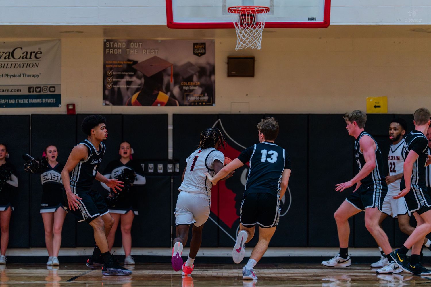 Basketball player in white jersey #1 drives past defenders during high school indoor gymnasium game.