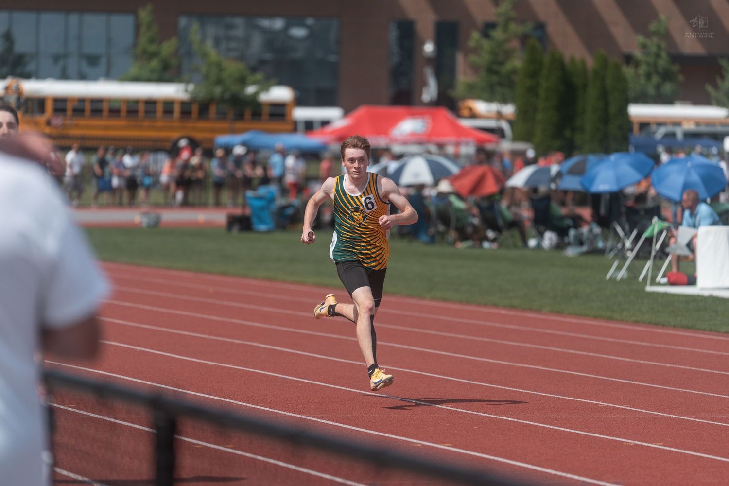 Young male runner competes in outdoor track race wearing gold and black uniform on red track.