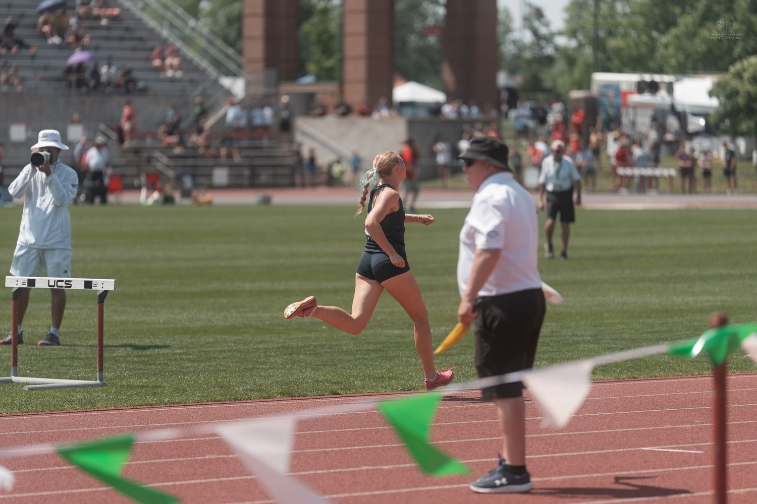 Female athlete running past hurdle at outdoor collegiate track and field competition.