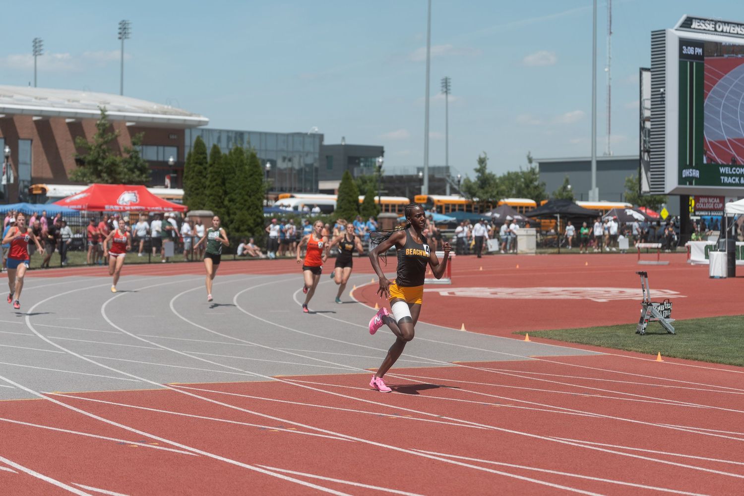 Athlete sprinting ahead of competitors on a red track during an outdoor high school track and field meet.