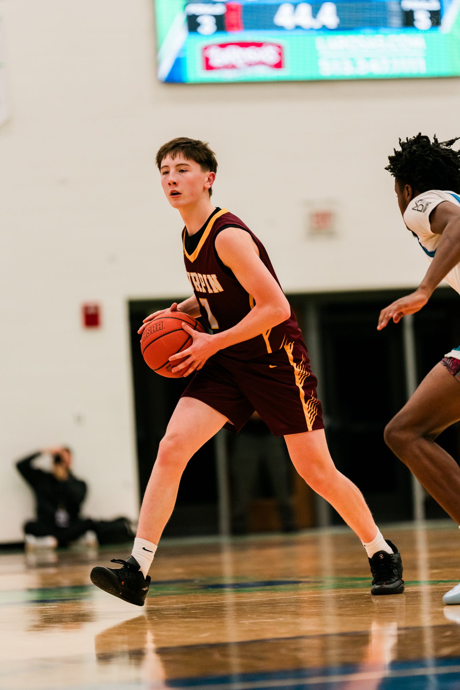 Turpin high school basketball player in maroon uniform handles the ball during a game.