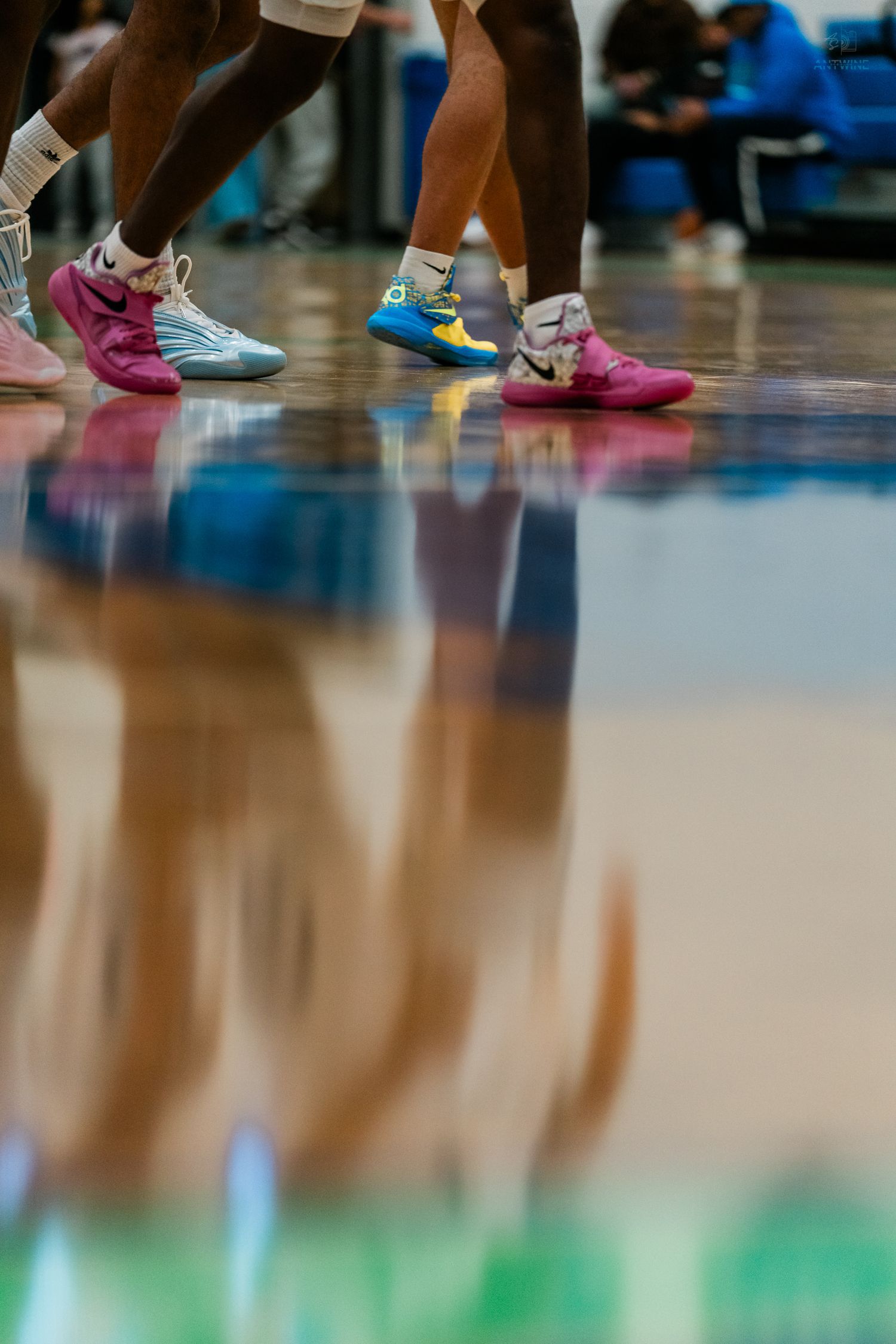 Basketball players wearing vibrant pink and teal Nike sneakers reflected on a glossy hardwood court.