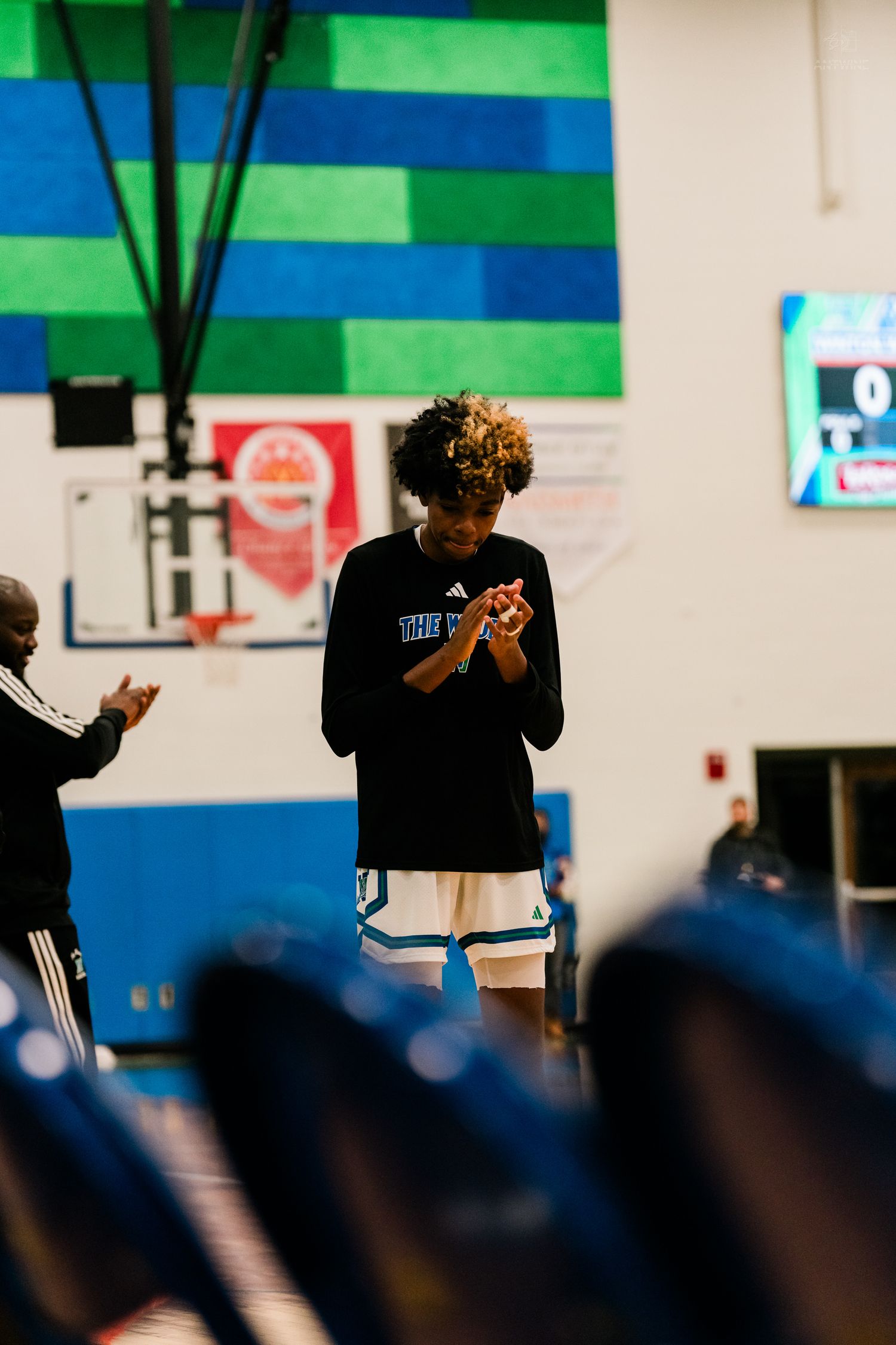Basketball player in black warmup claps hands on court before game.