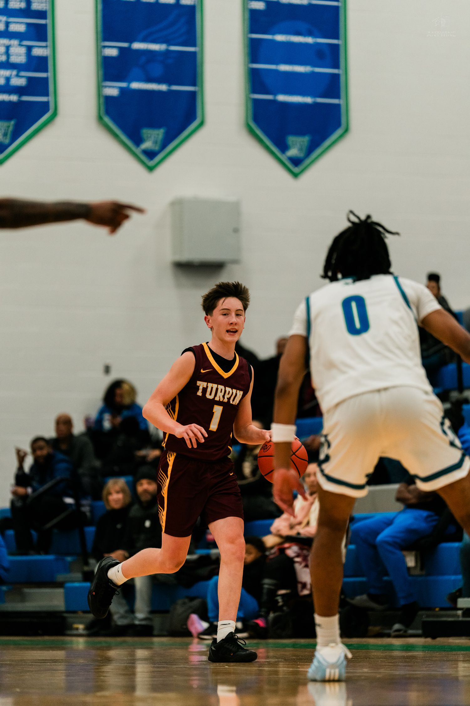 Turpin High School basketball player number 1 dribbles upcourt against defender in white number 0 jersey.