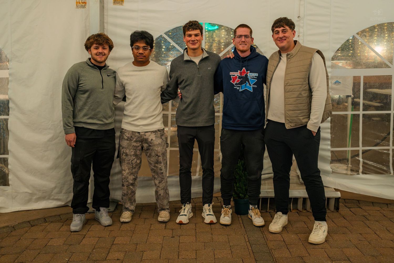 Five young men pose together smiling inside a white event tent.