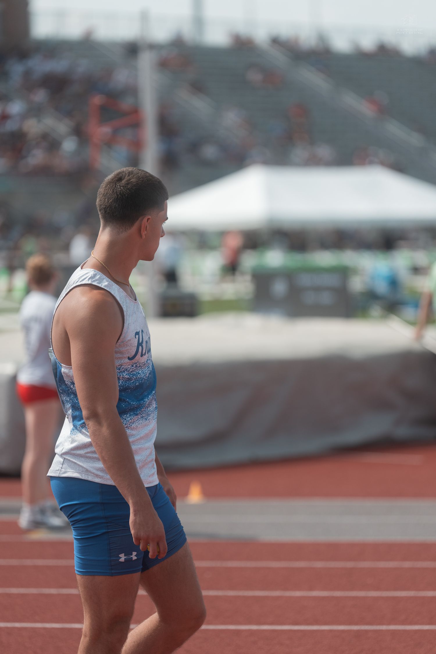 Male track athlete in Knights uniform and blue shorts stands on red track at outdoor competition.