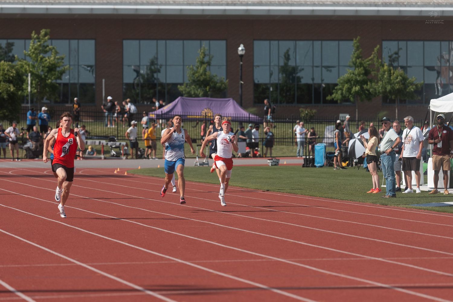 Track athletes race down the straightaway in a competitive high school outdoor track and field event.