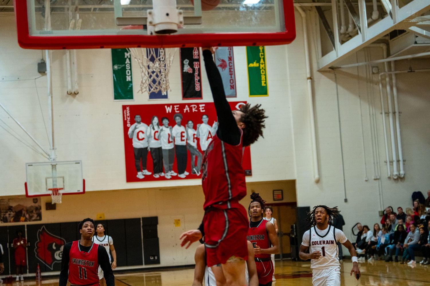 Basketball player leaps high for a dunk during a high school game with crowd watching.