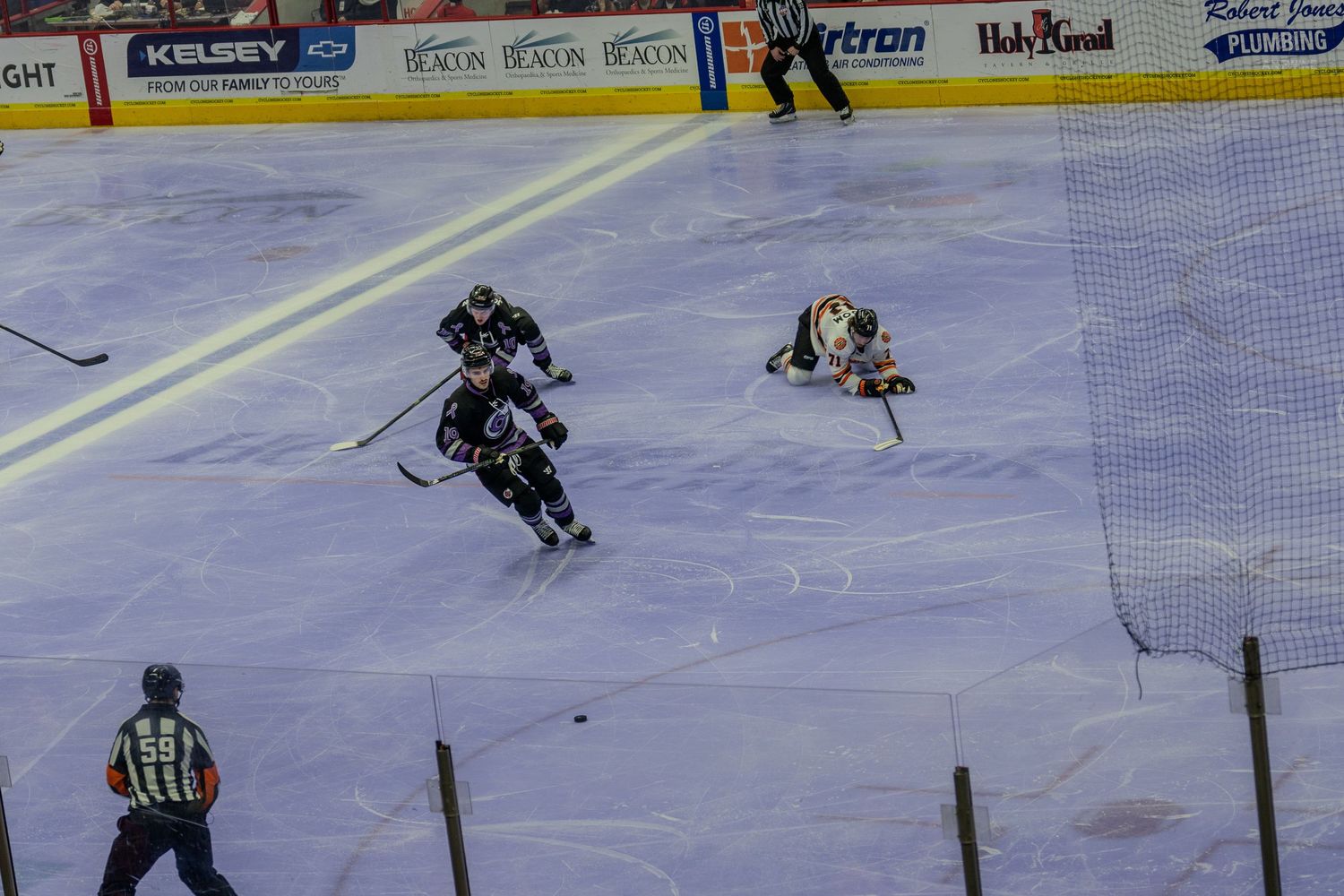 Minor league hockey players battle near the goal as a goalie makes a save during an intense game.