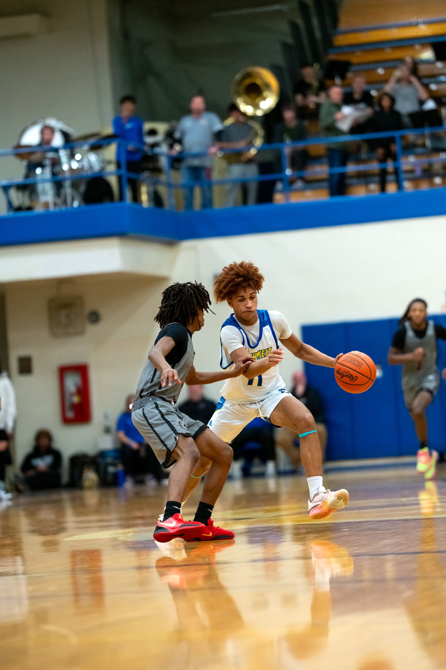 High school basketball player #11 drives past defender during competitive game with crowd watching.