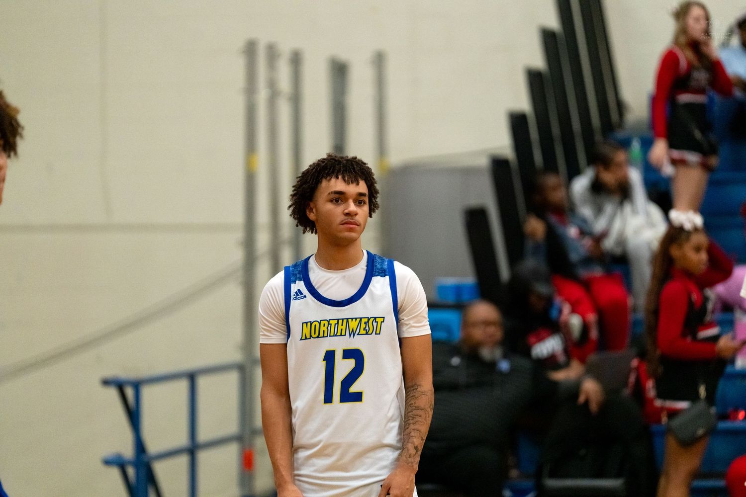 Close-up portrait of high school basketball player #12 in a blue and gold uniform on the court.