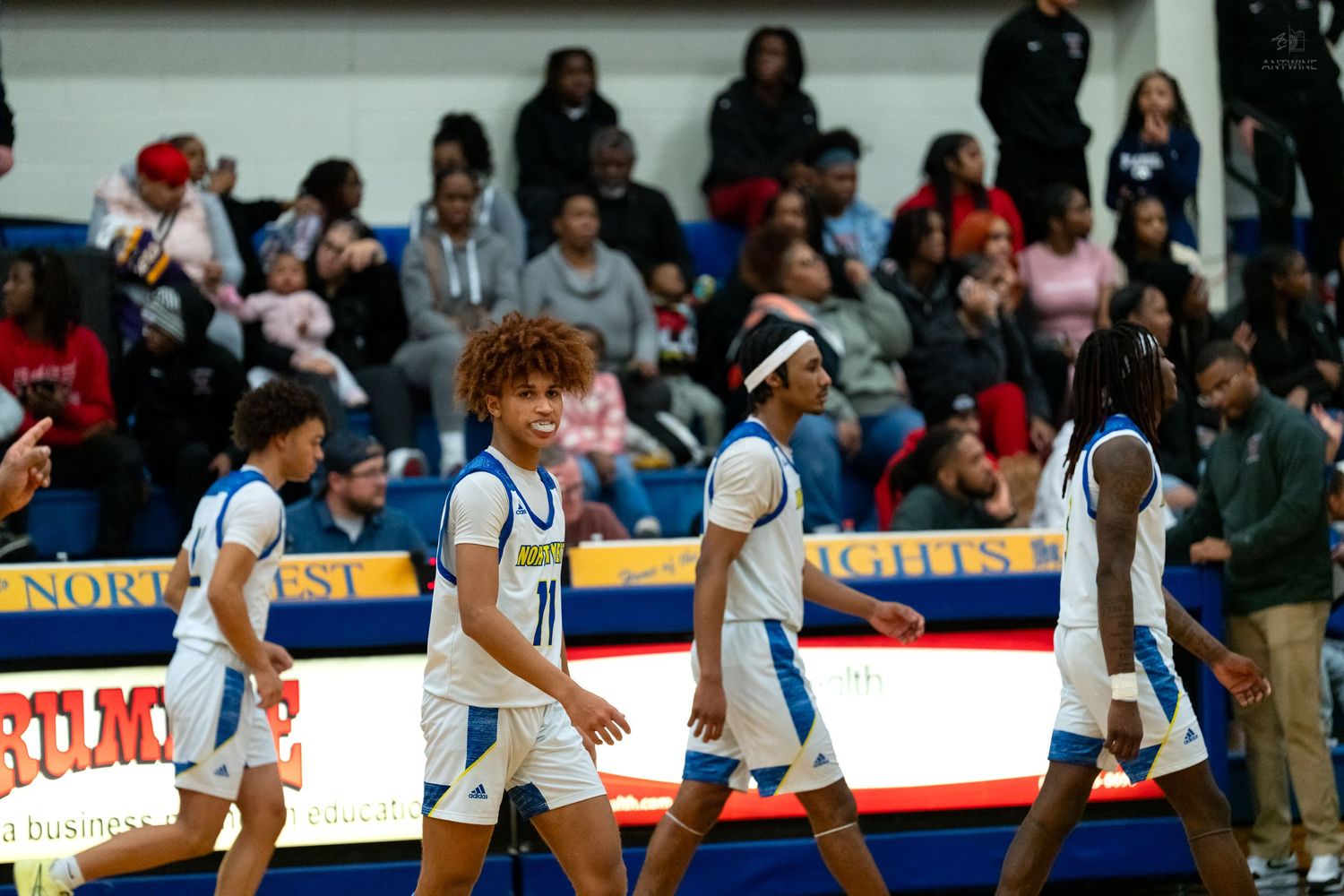 Northwest Knights basketball players walk on court during a home game with fans cheering in packed gymnasium bleachers.