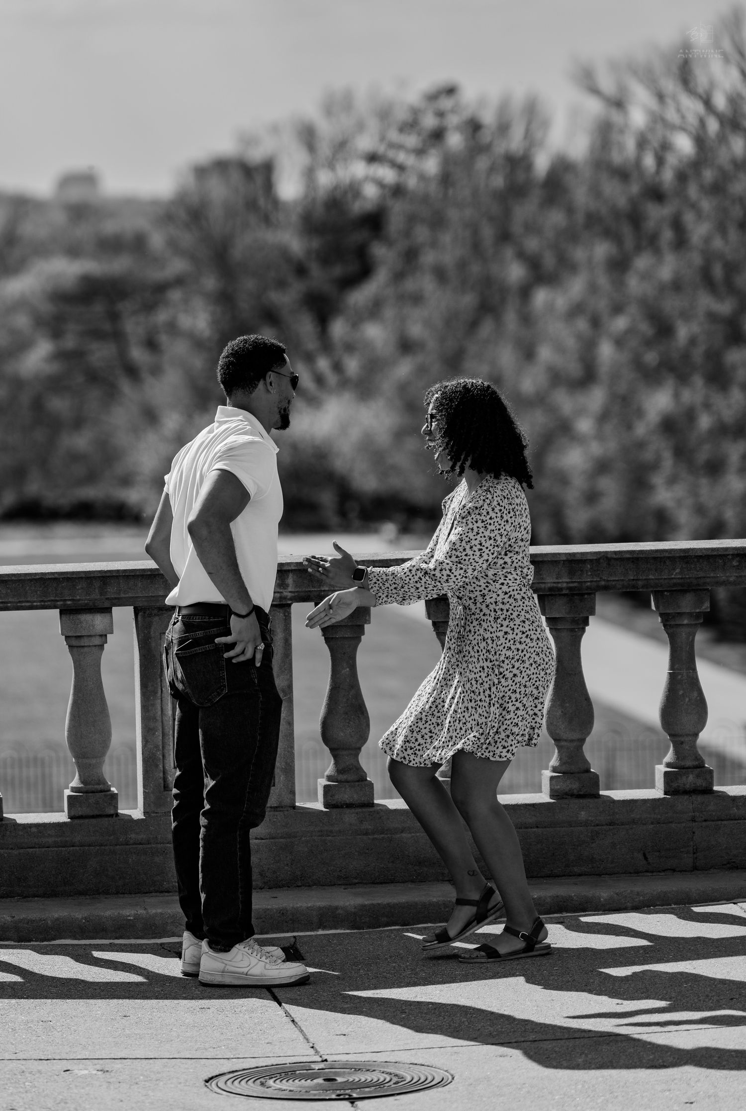 Black and white photo of a joyful couple holding hands and celebrating on a sunlit stone terrace.
