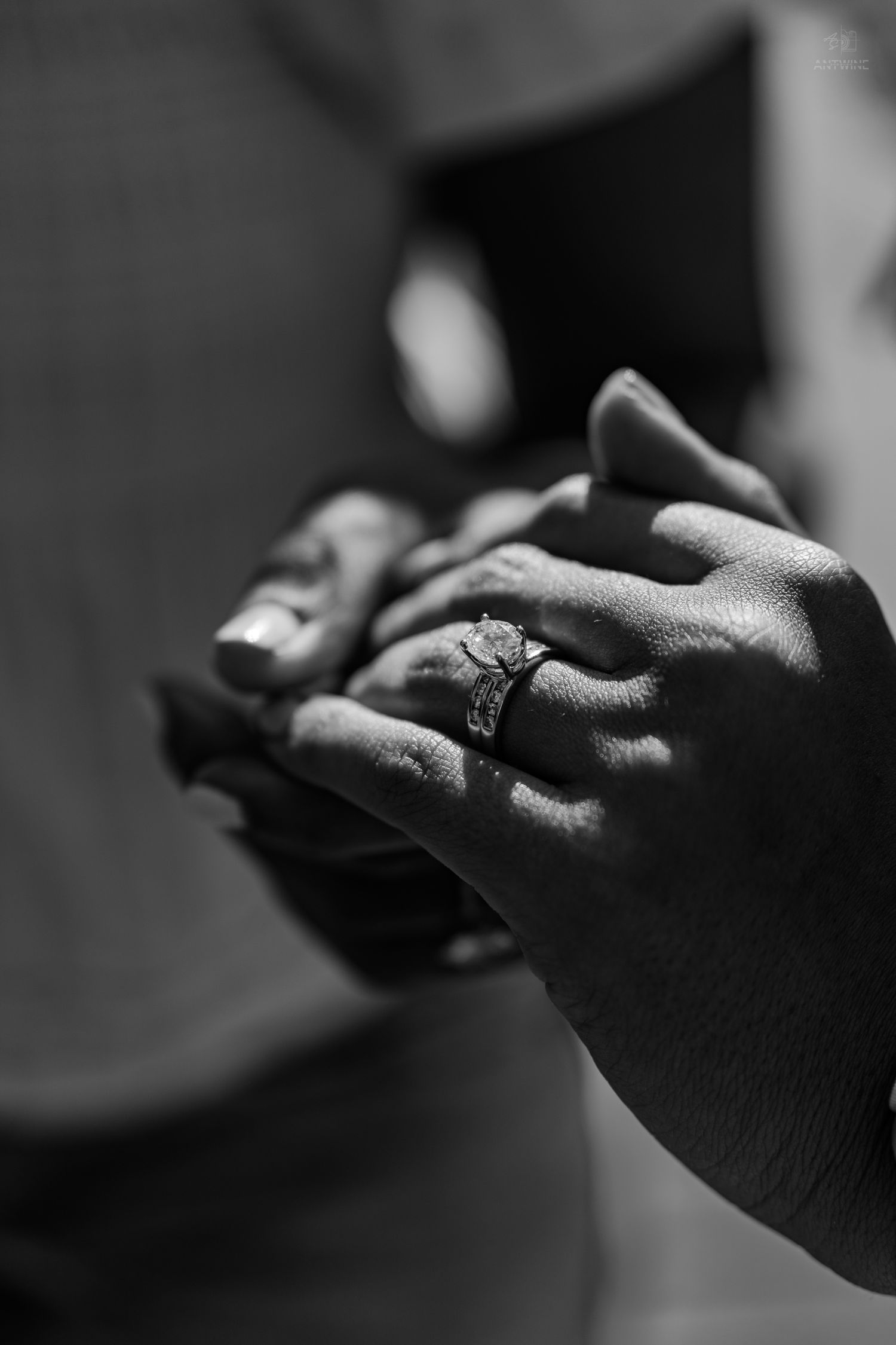 Close-up black and white photo of two hands clasped together showing a diamond engagement ring.