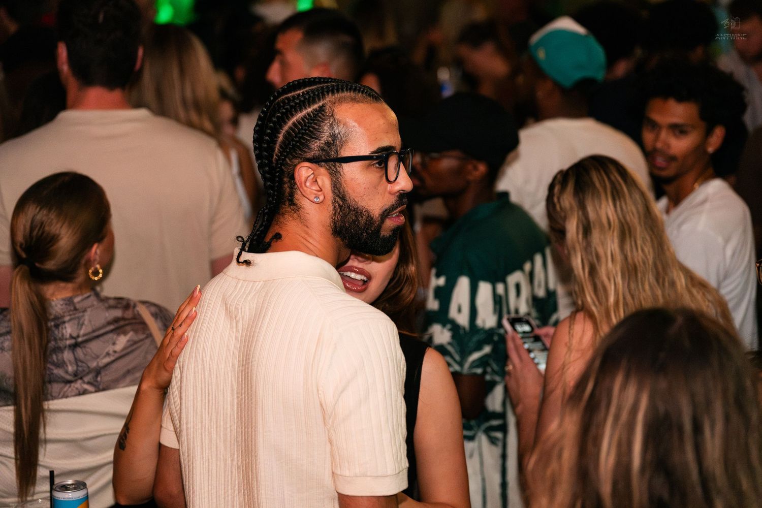 Smiling man with braided hair and glasses socializing at a lively nightclub party.
