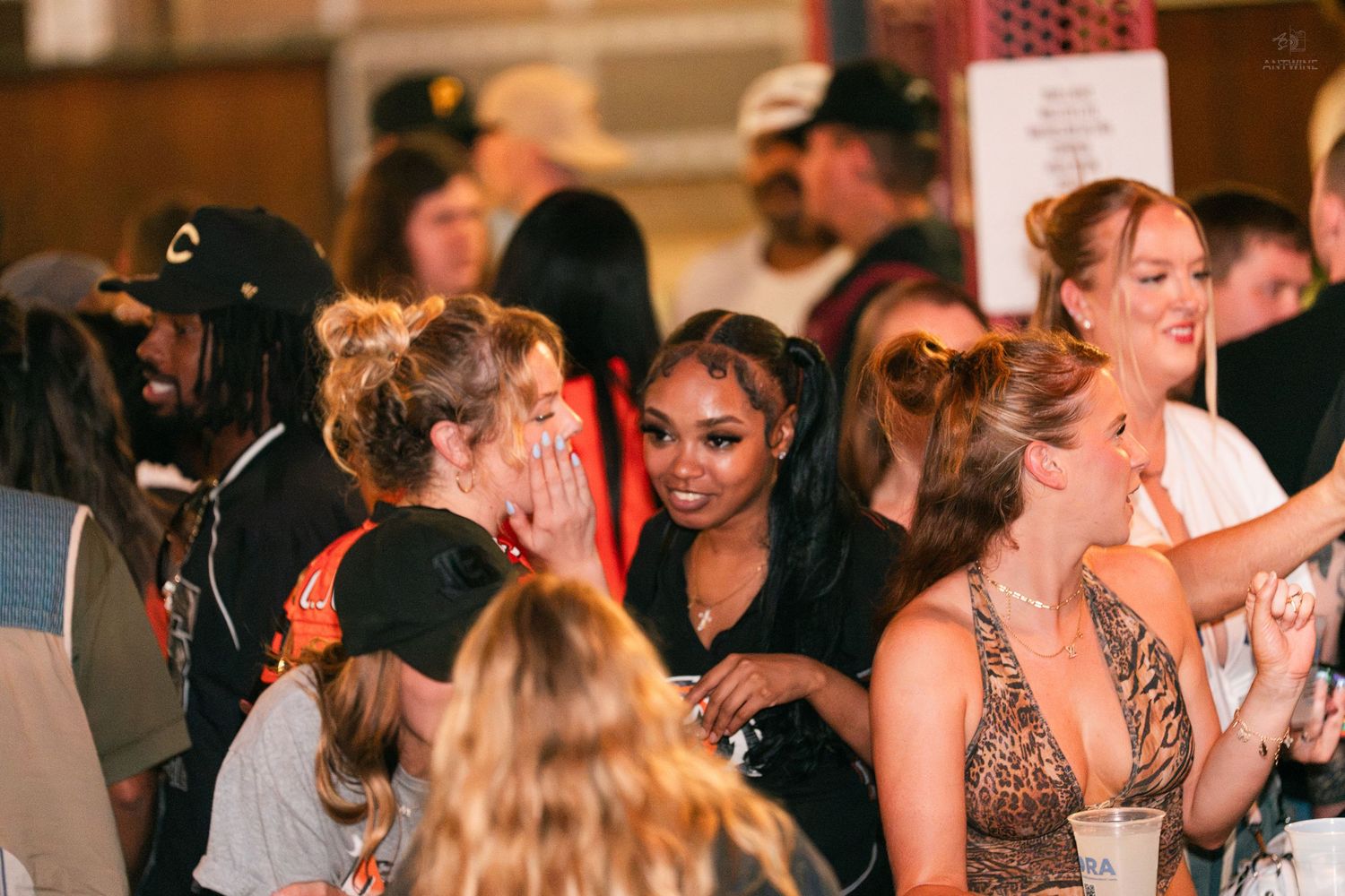 Group of women smiling and socializing together at a crowded indoor party event.