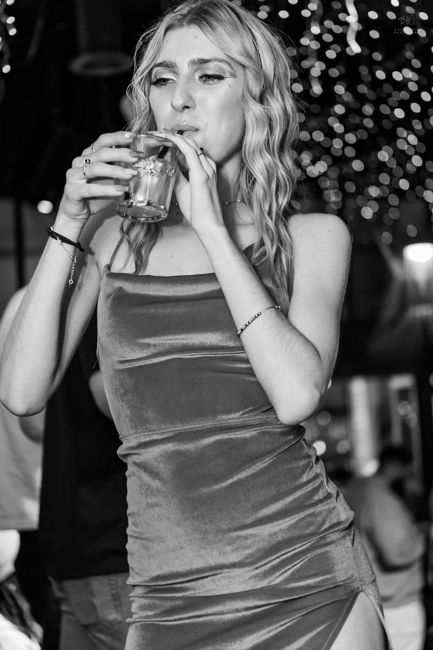 Blonde woman in a velvet dress sipping a drink at a nightclub event.