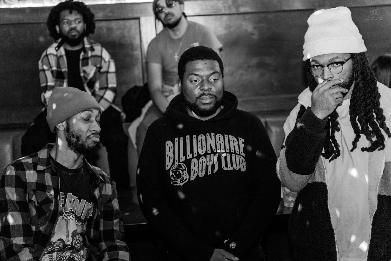 Black and white photo of men posing in a venue, featuring one in a Billionaire Boys Club sweatshirt.