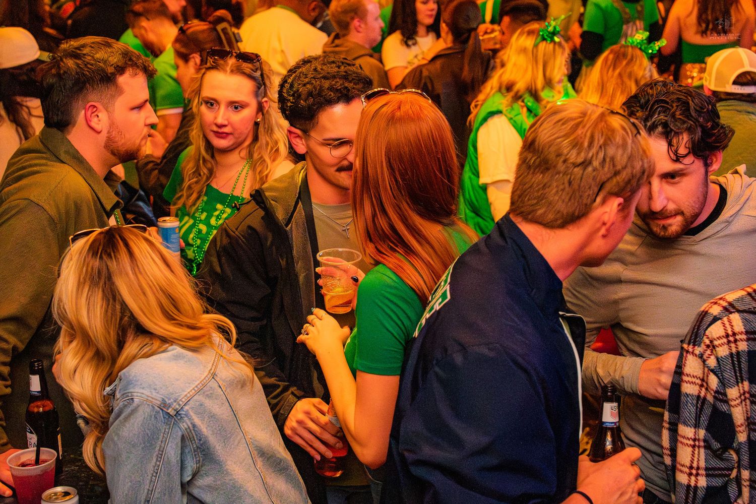 Group of young adults socializing and mingling at a St. Patrick's Day bar event.
