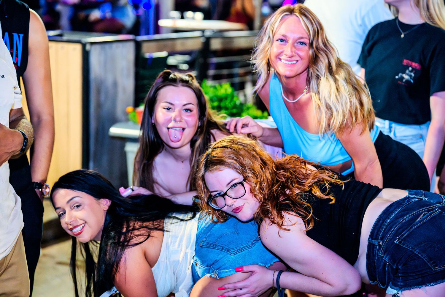 Group of four women laughing and goofing around together inside a bar.