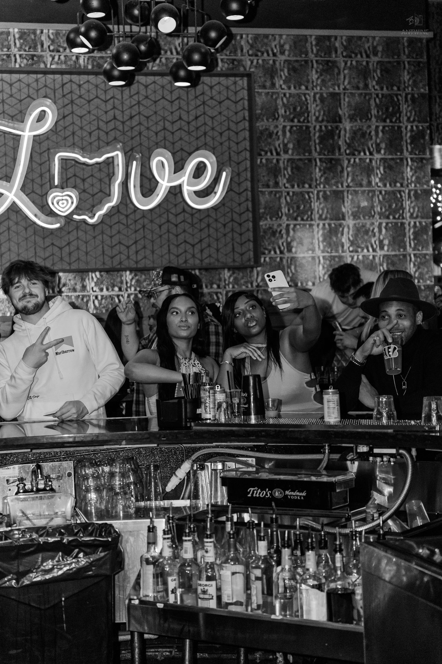 Black and white photo of friends posing at a bar under a neon Love Ohio sign.