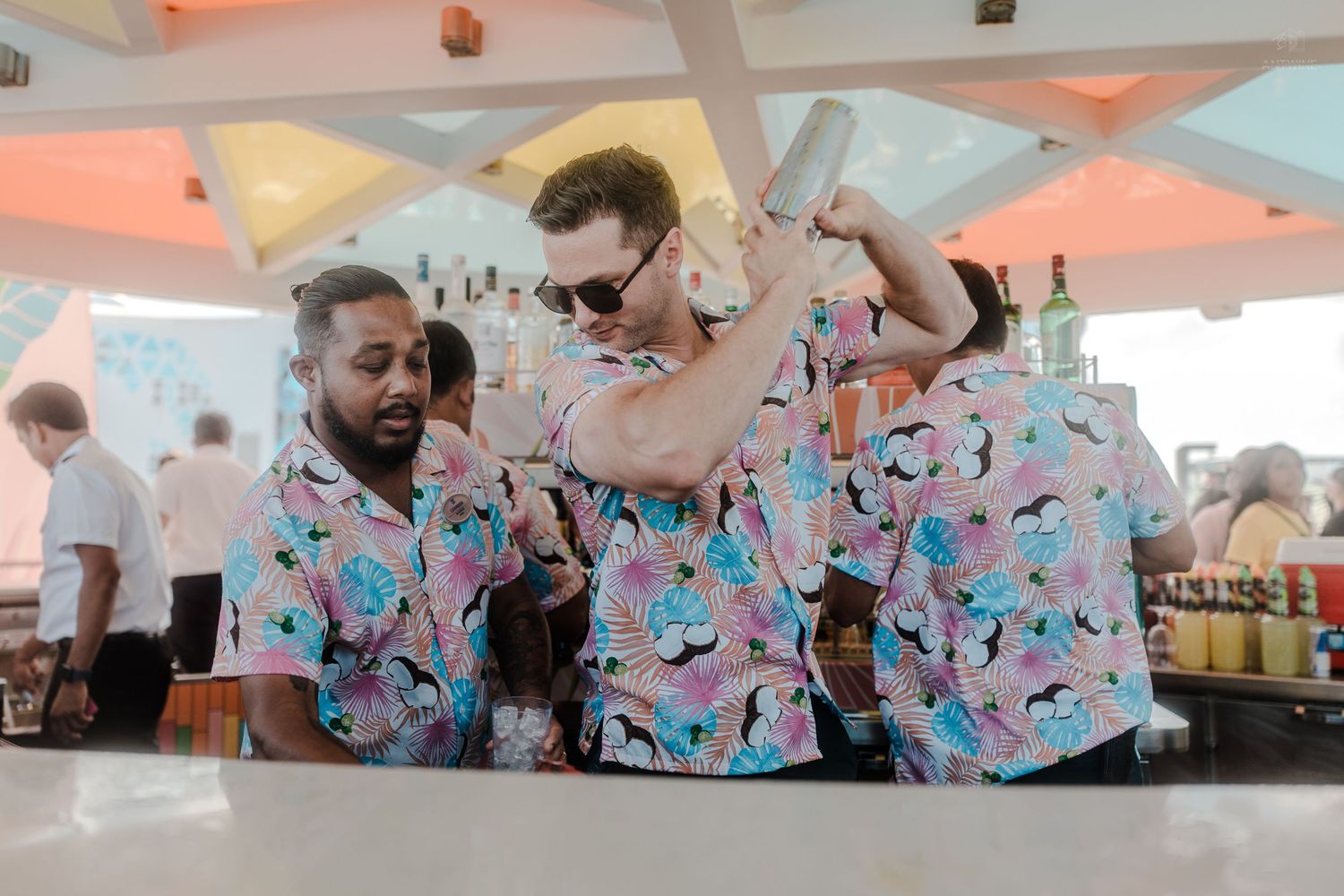 Three bartenders in matching floral shirts mixing cocktails at an outdoor bar.