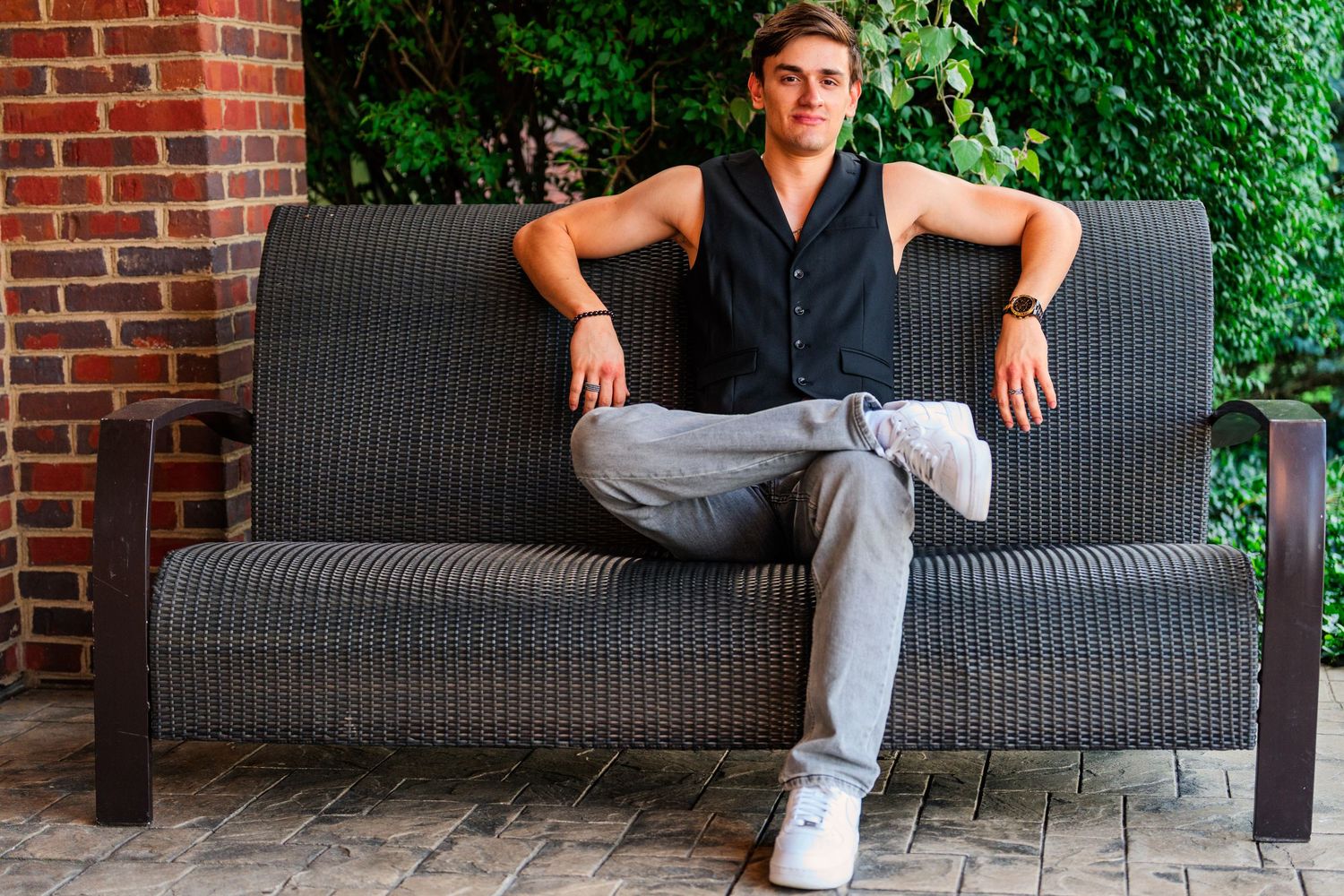 Young man relaxing on outdoor wicker sofa near brick wall and green ivy.