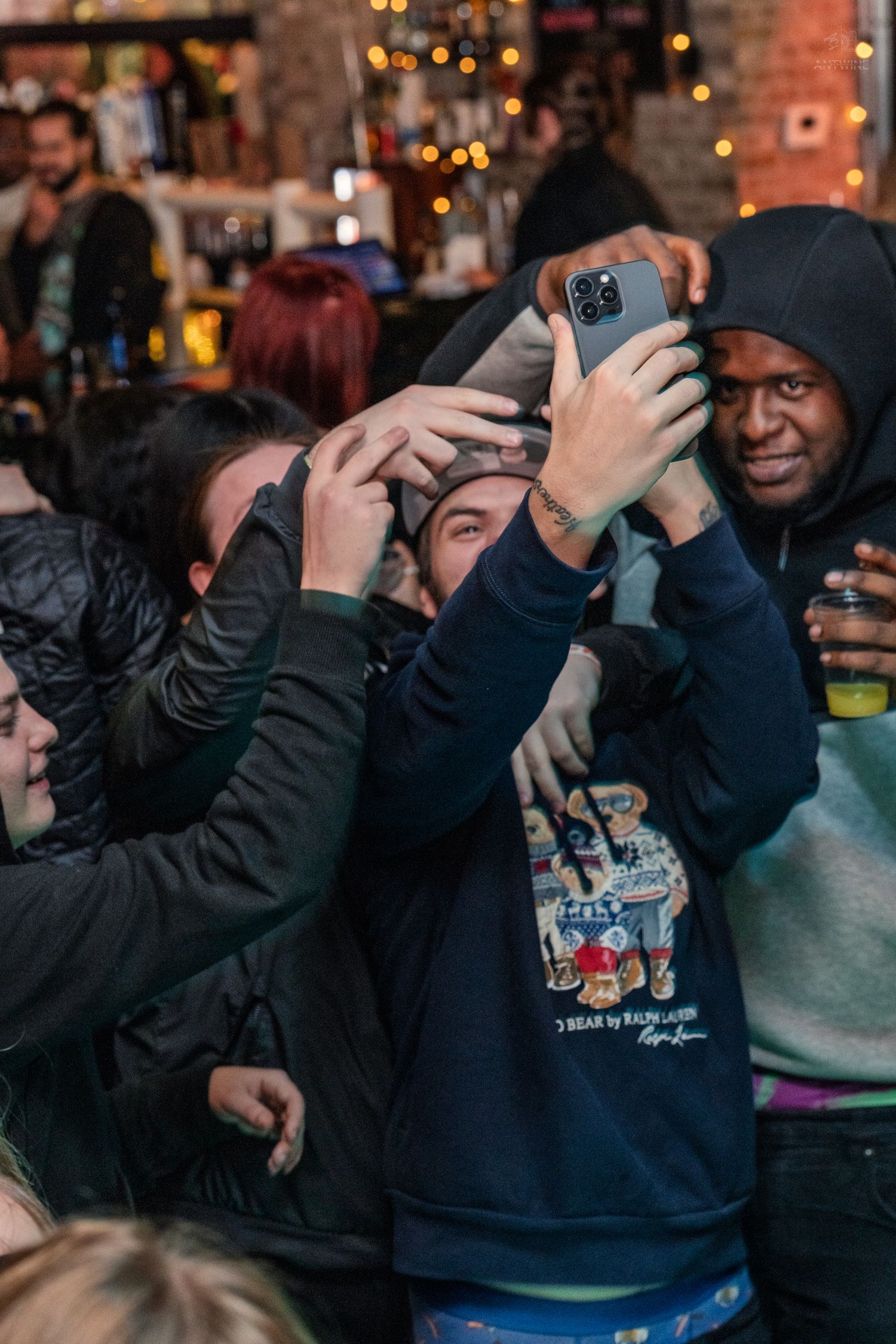 Group of people taking selfies with smartphones at a lively bar event.