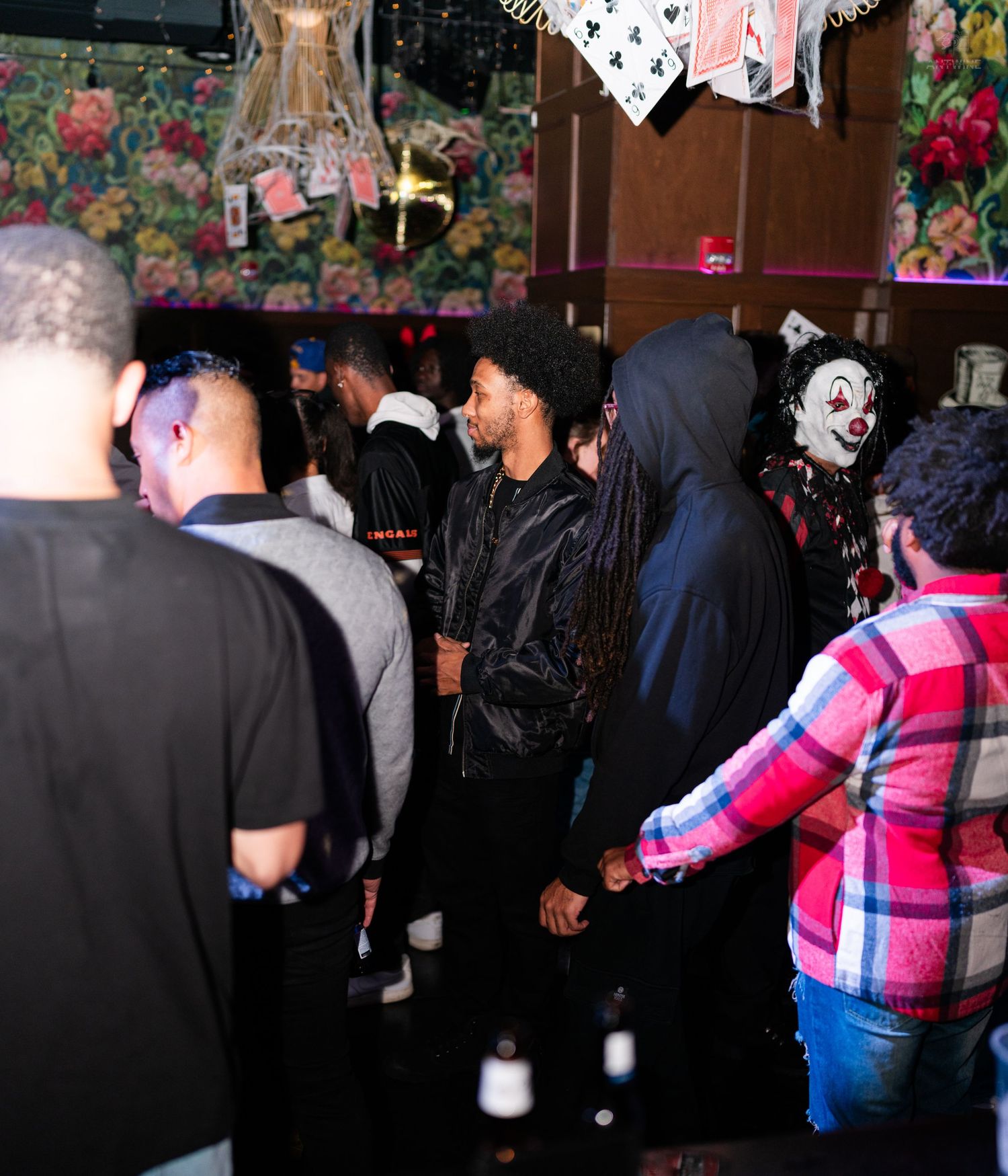 Diverse crowd at a Halloween party with a clown costume visible in background.