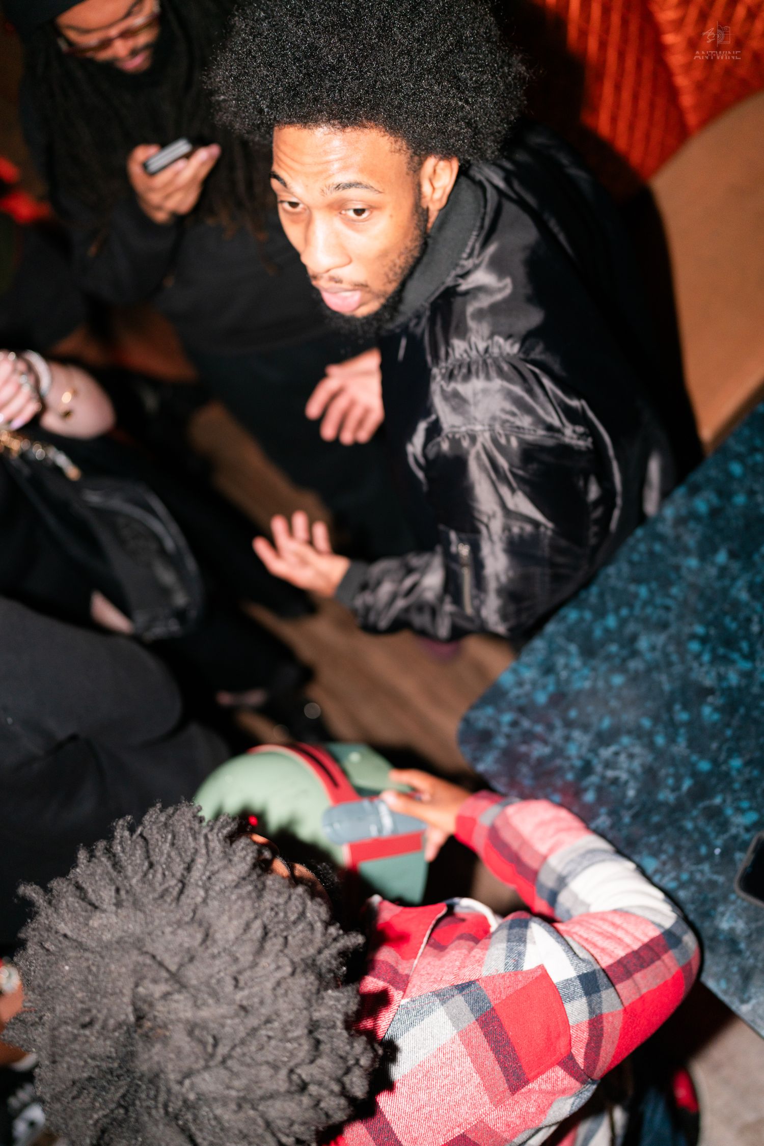Man in black jacket looks up at camera during a crowded Halloween costume party event.