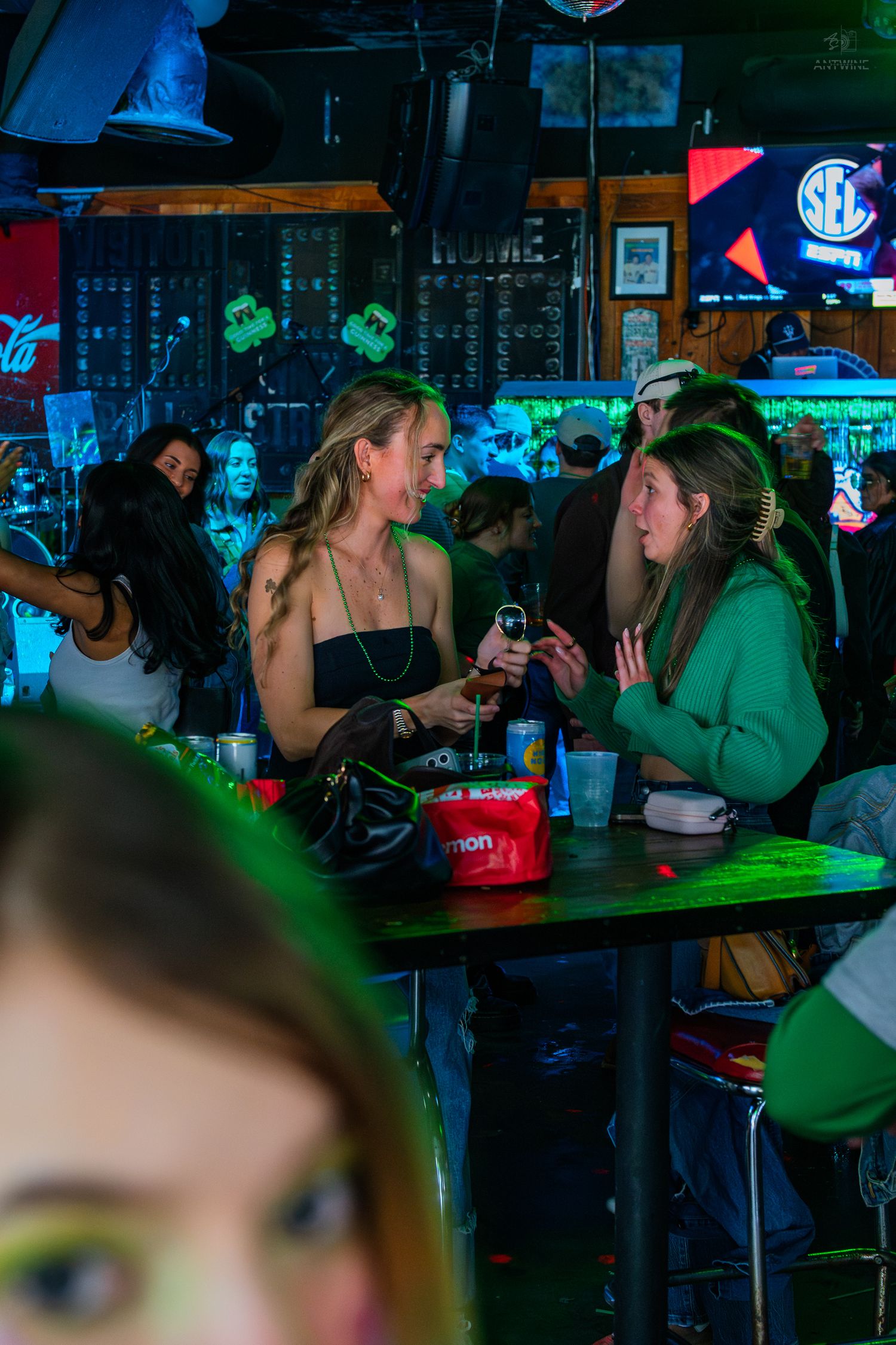Two women socializing at a lively bar decorated in green for St. Patrick's Day celebrations.