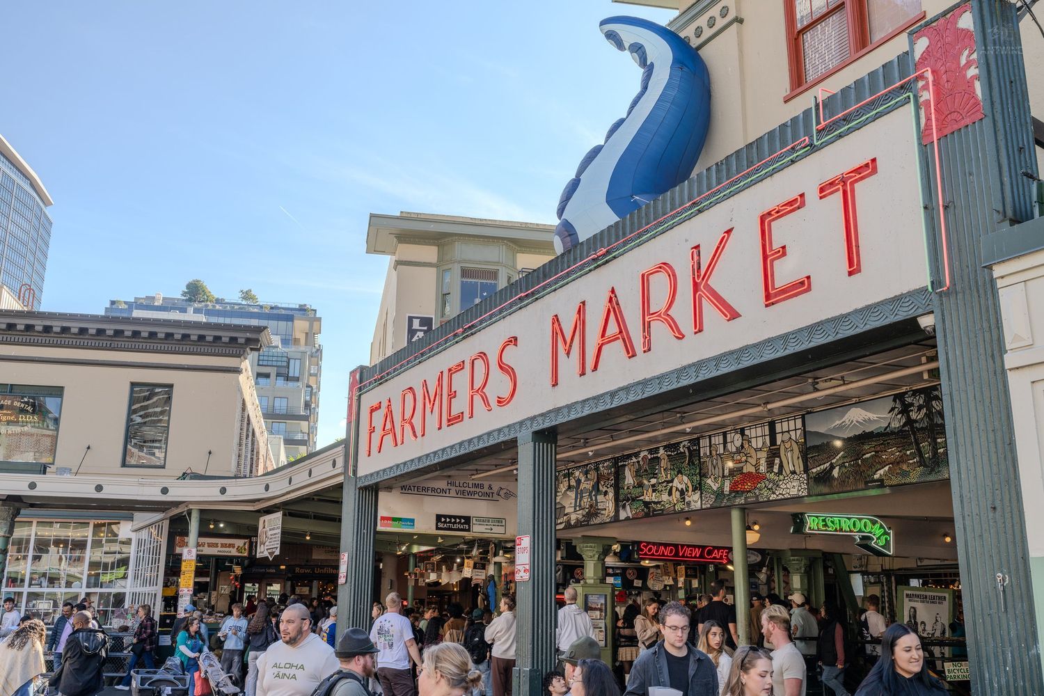 Seattle Pike Place Farmers Market entrance with iconic blue fish sign and crowds of shoppers.