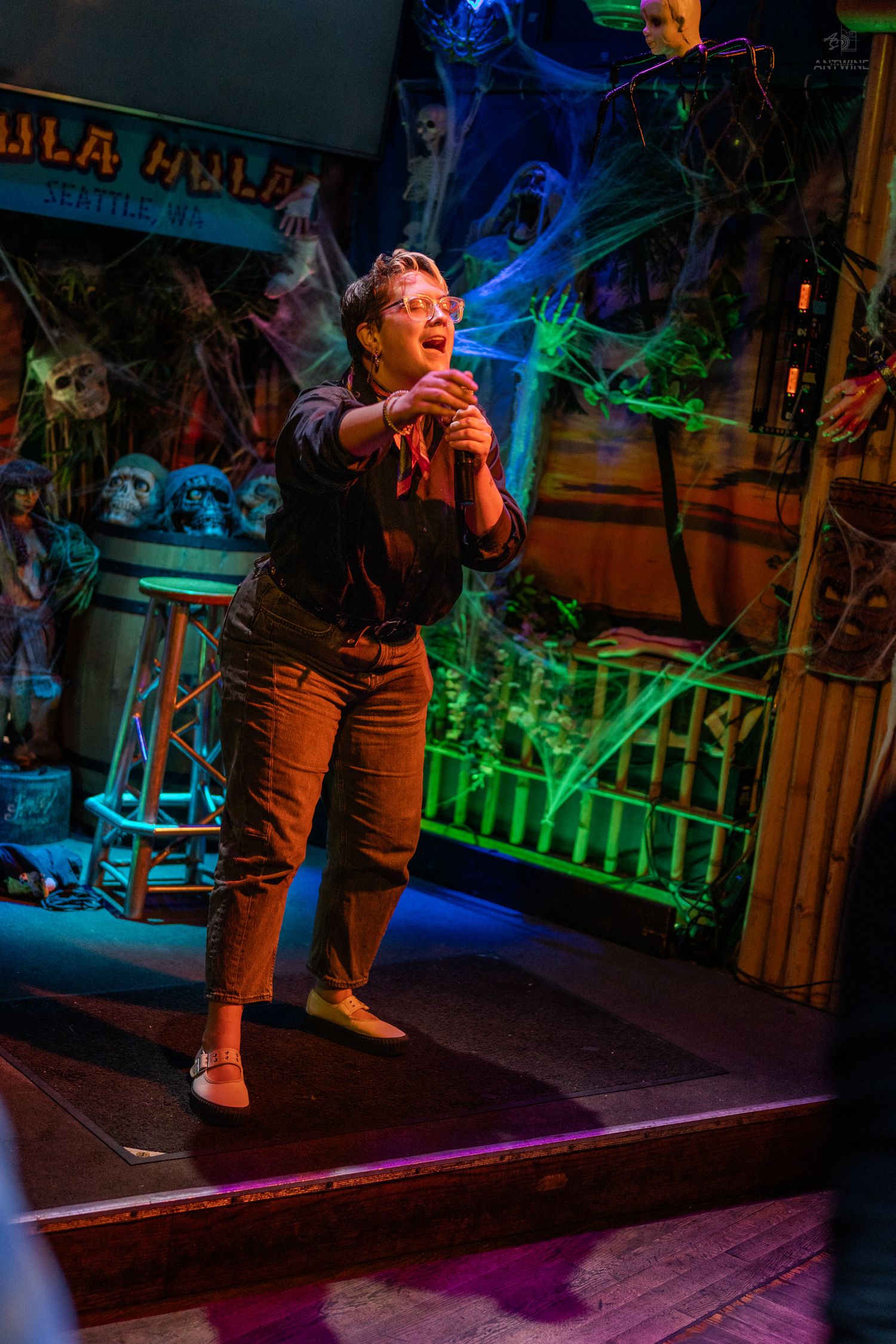 Woman singing on stage at a Halloween-themed karaoke bar with spooky decorations and green laser lights.