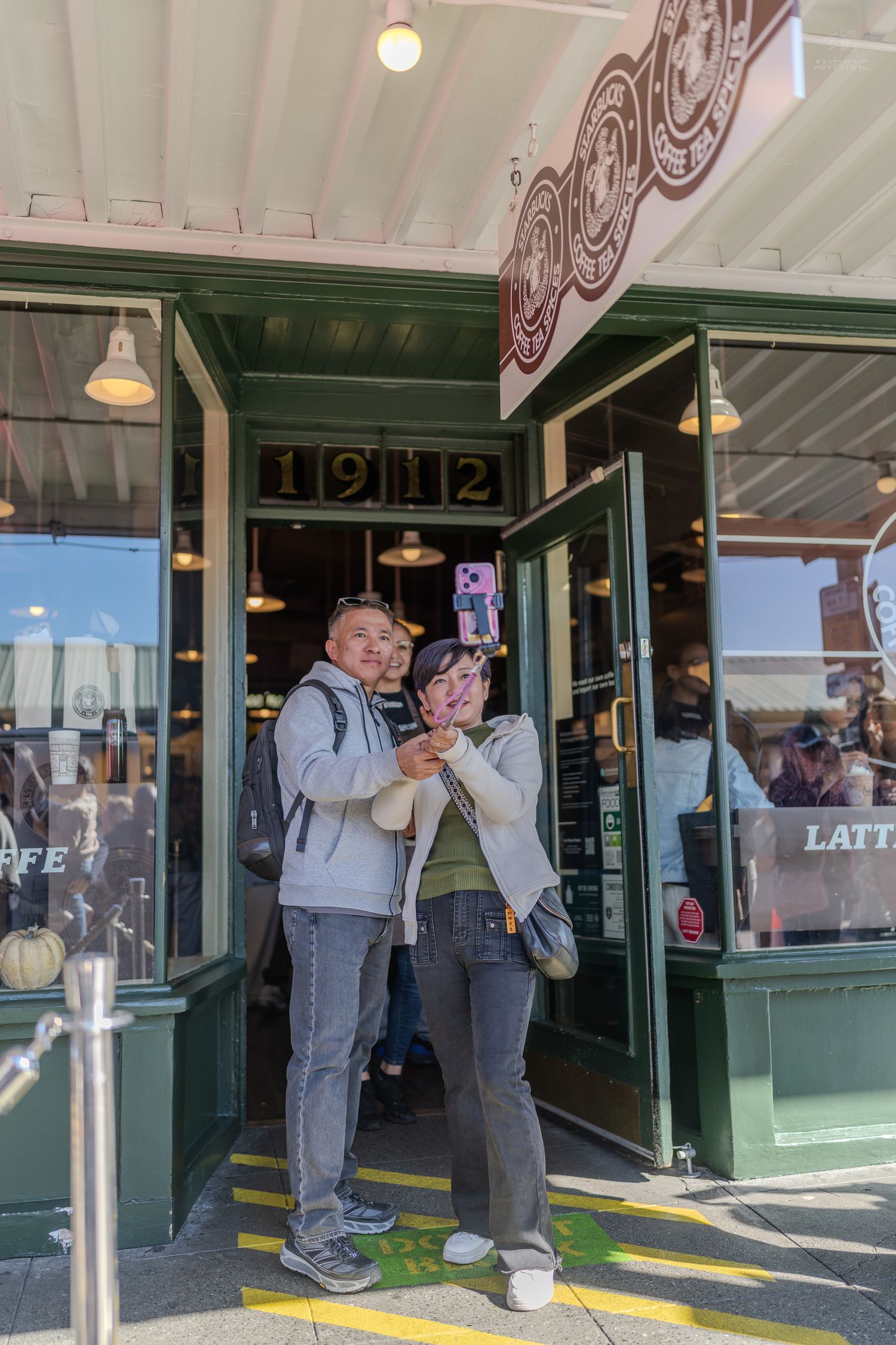 A couple taking a selfie outside the historic 1912 original Starbucks at Pike Place Market in Seattle.
