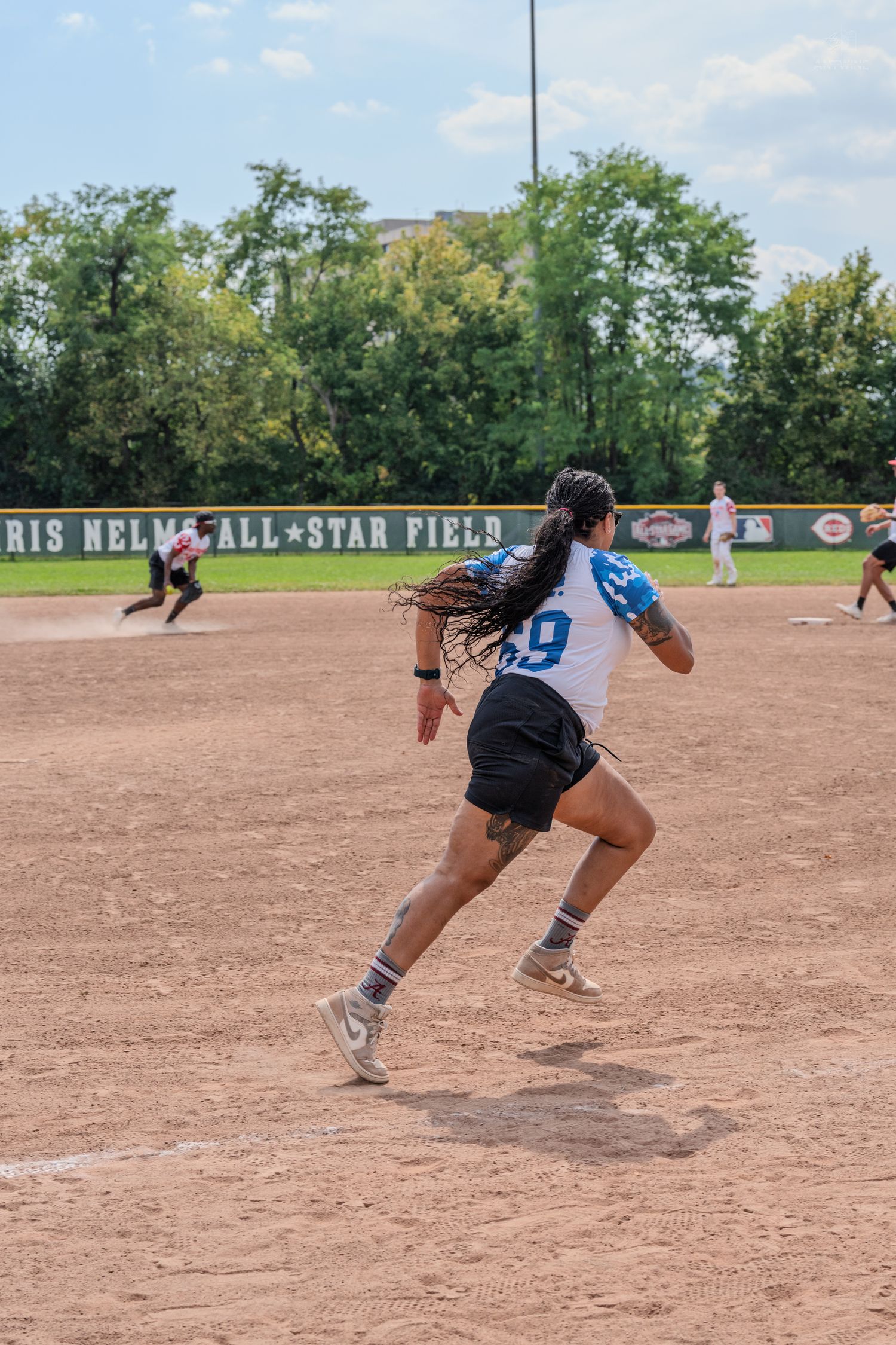 Female softball player wearing number 9 runs the bases at Chris Nelms All-Star Field during a game.