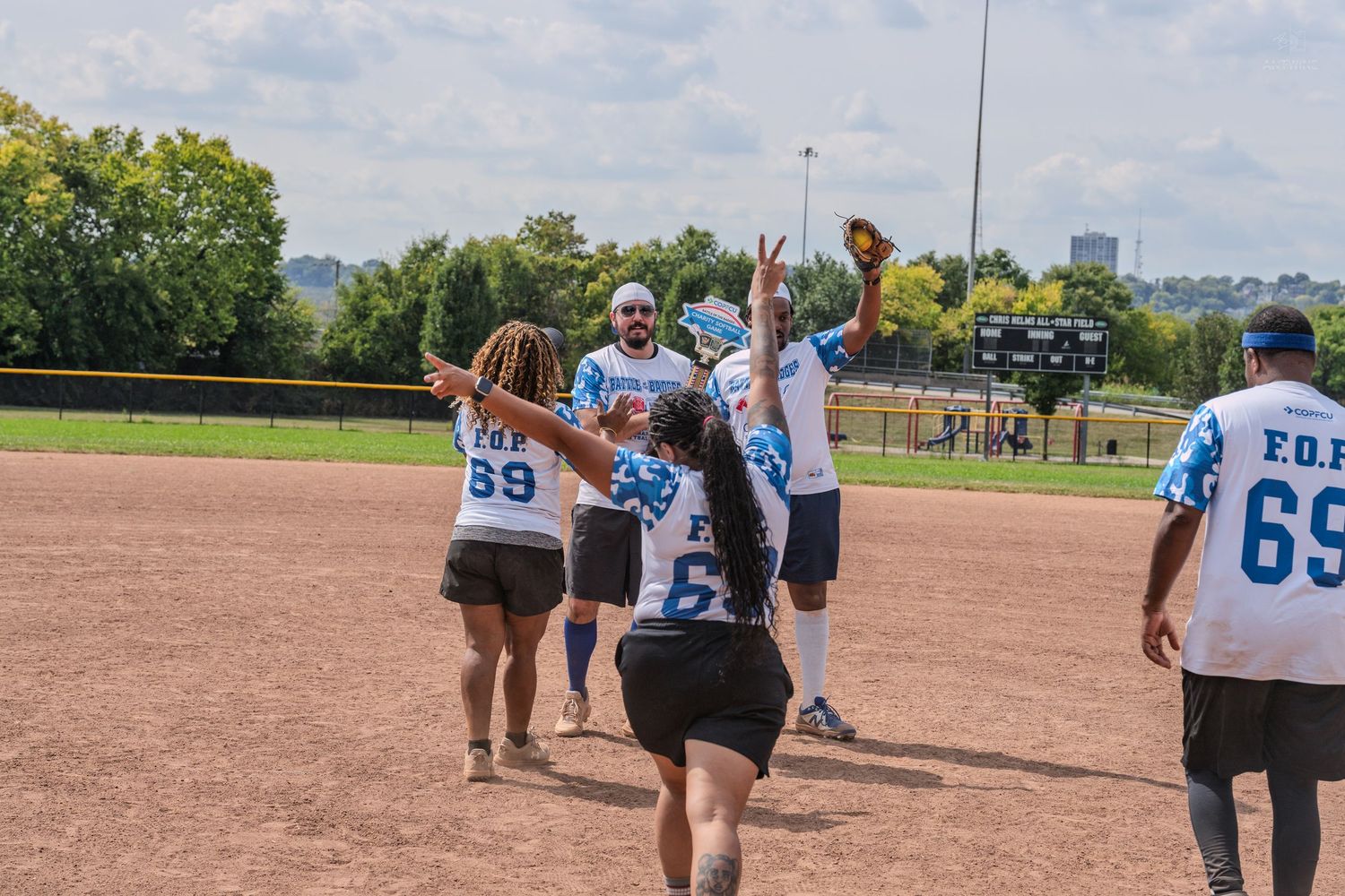 A team of softball players in blue and white jerseys celebrate together on a dirt baseball field after a game.