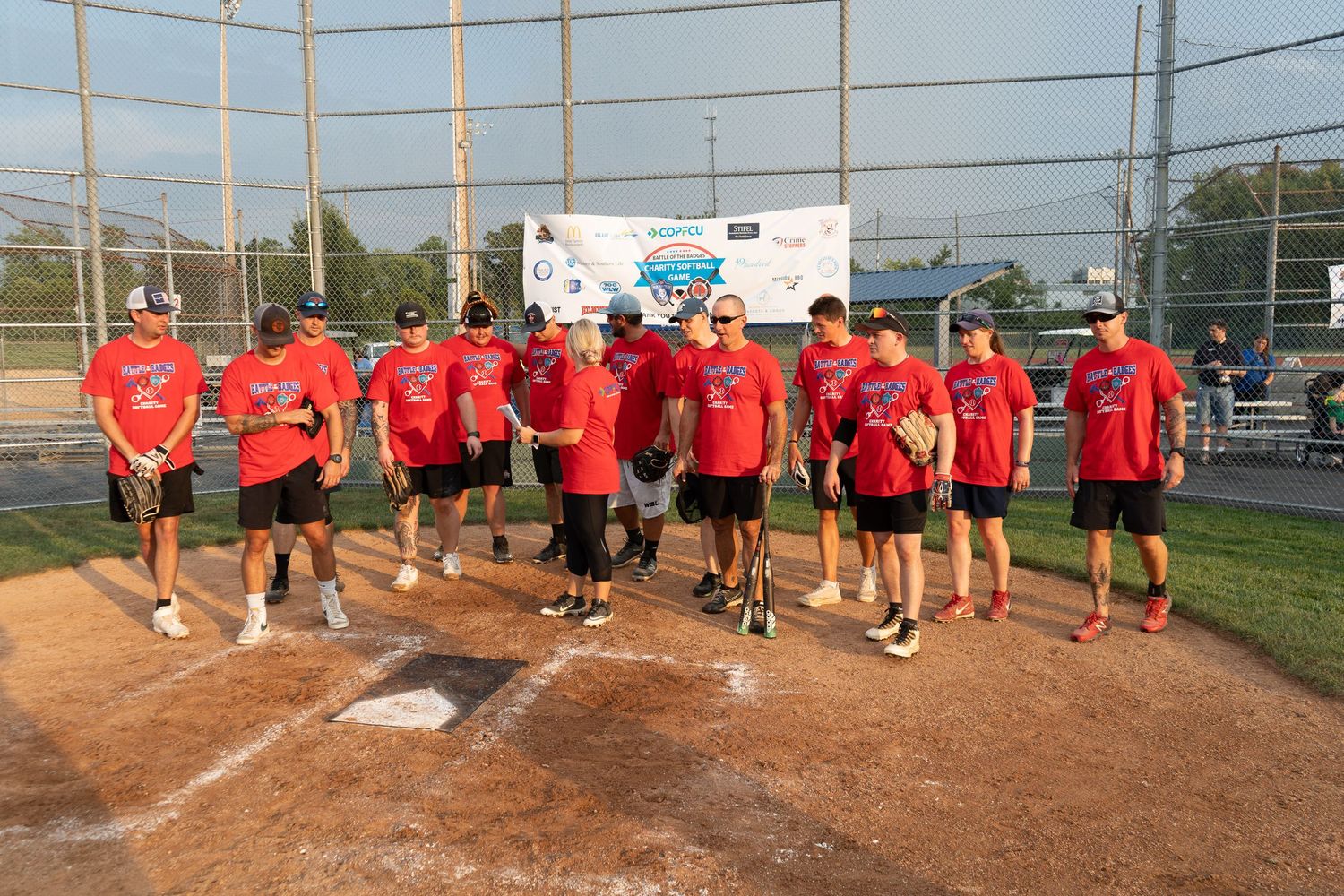 Team in red uniforms poses together at home plate during a charity softball game.