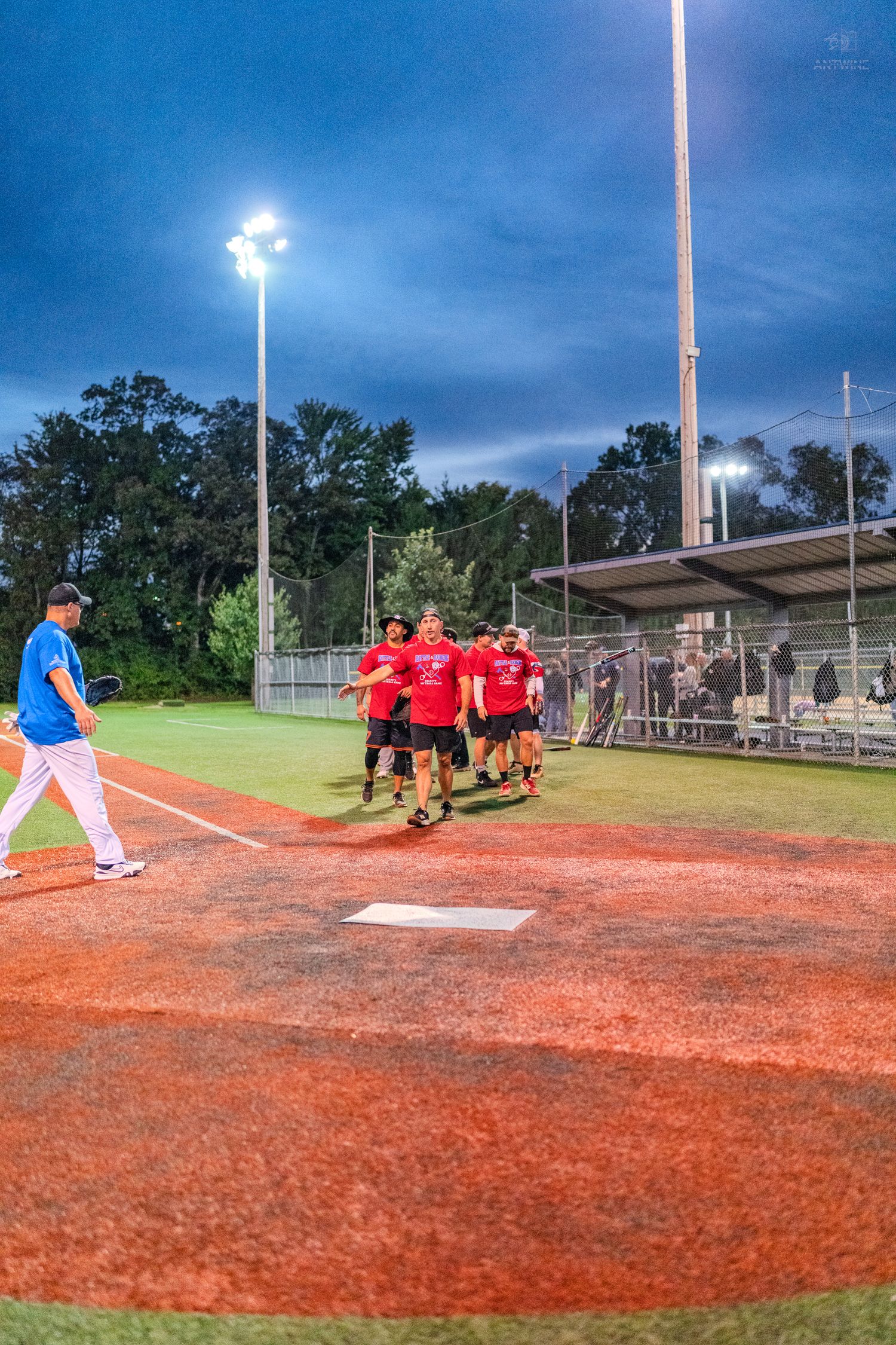 Red-shirted softball team celebrates victory walking off illuminated field at night under stadium lights.