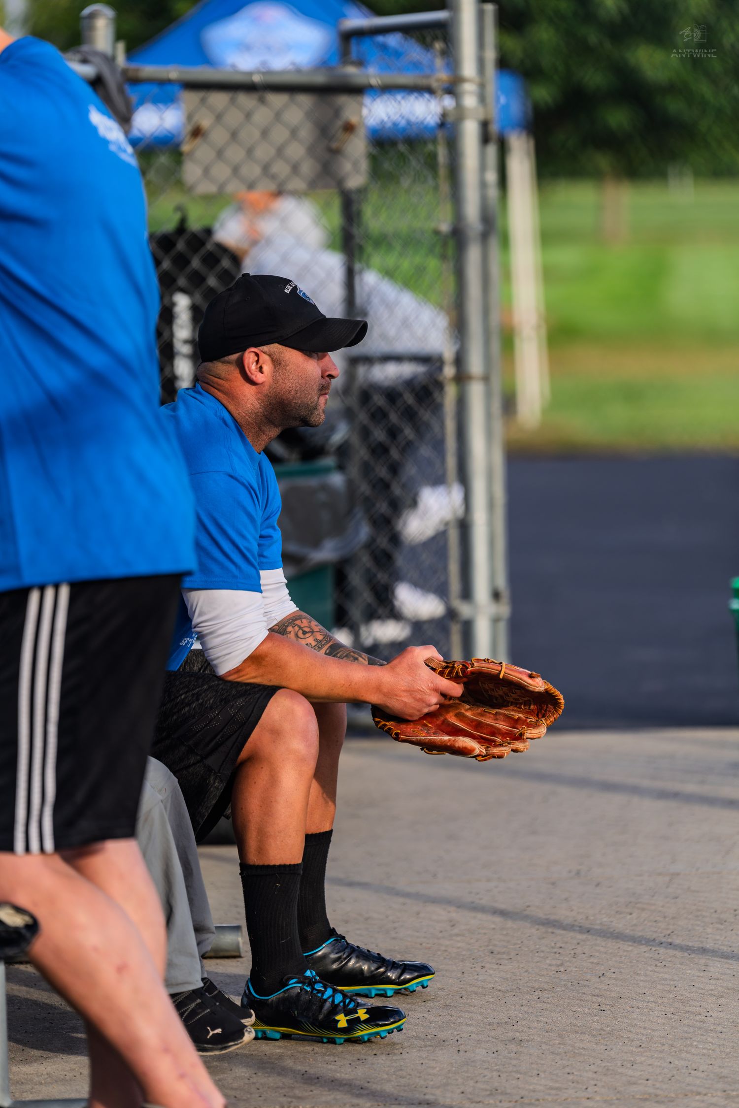 Baseball player in blue team uniform sitting in dugout holding a leather mitt before a game.