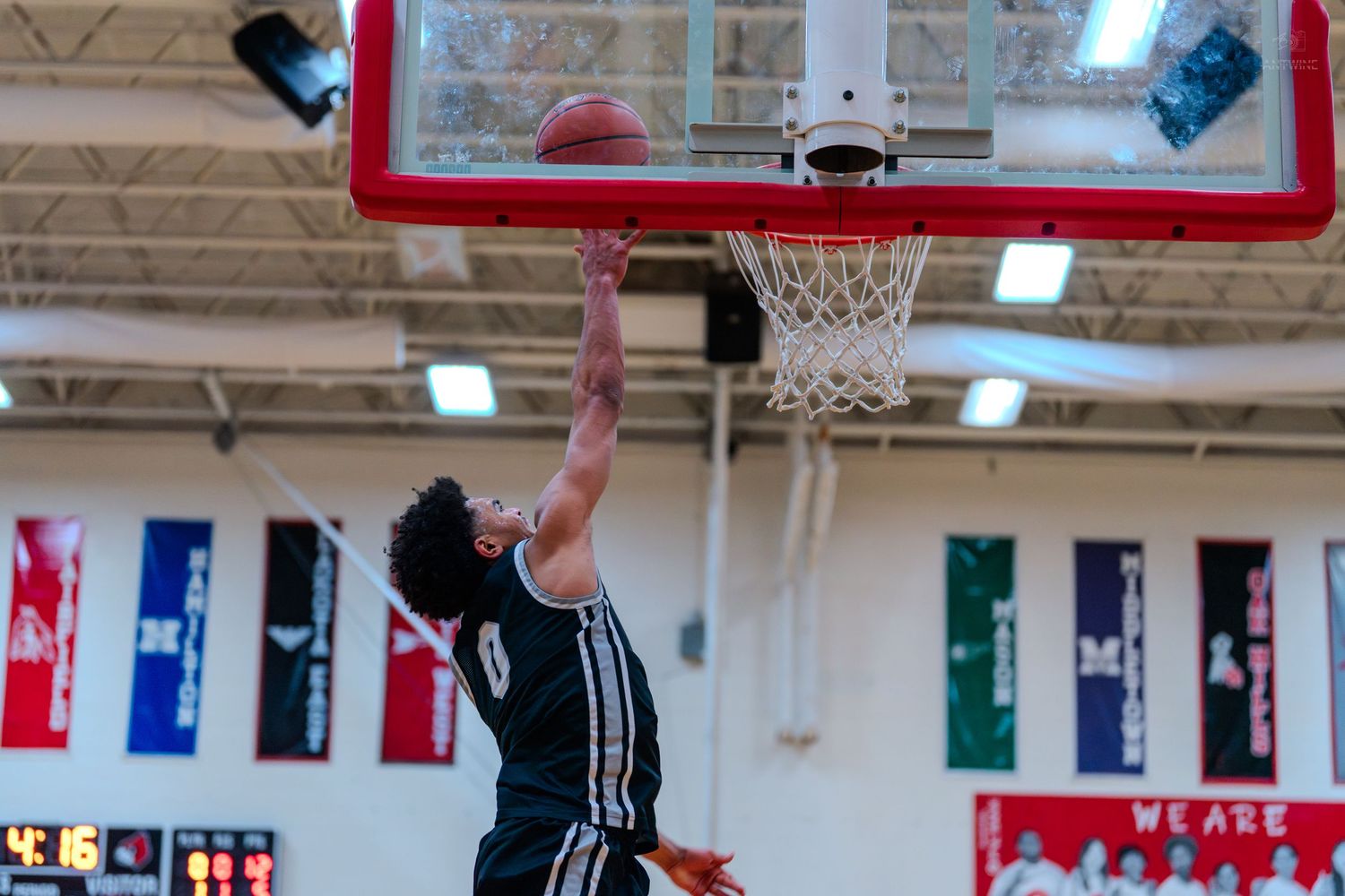 Basketball player in black jersey #0 executes powerful slam dunk during indoor high school game.
