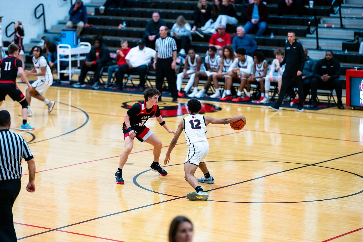Player #12 faces defender during competitive high school basketball game on indoor court.