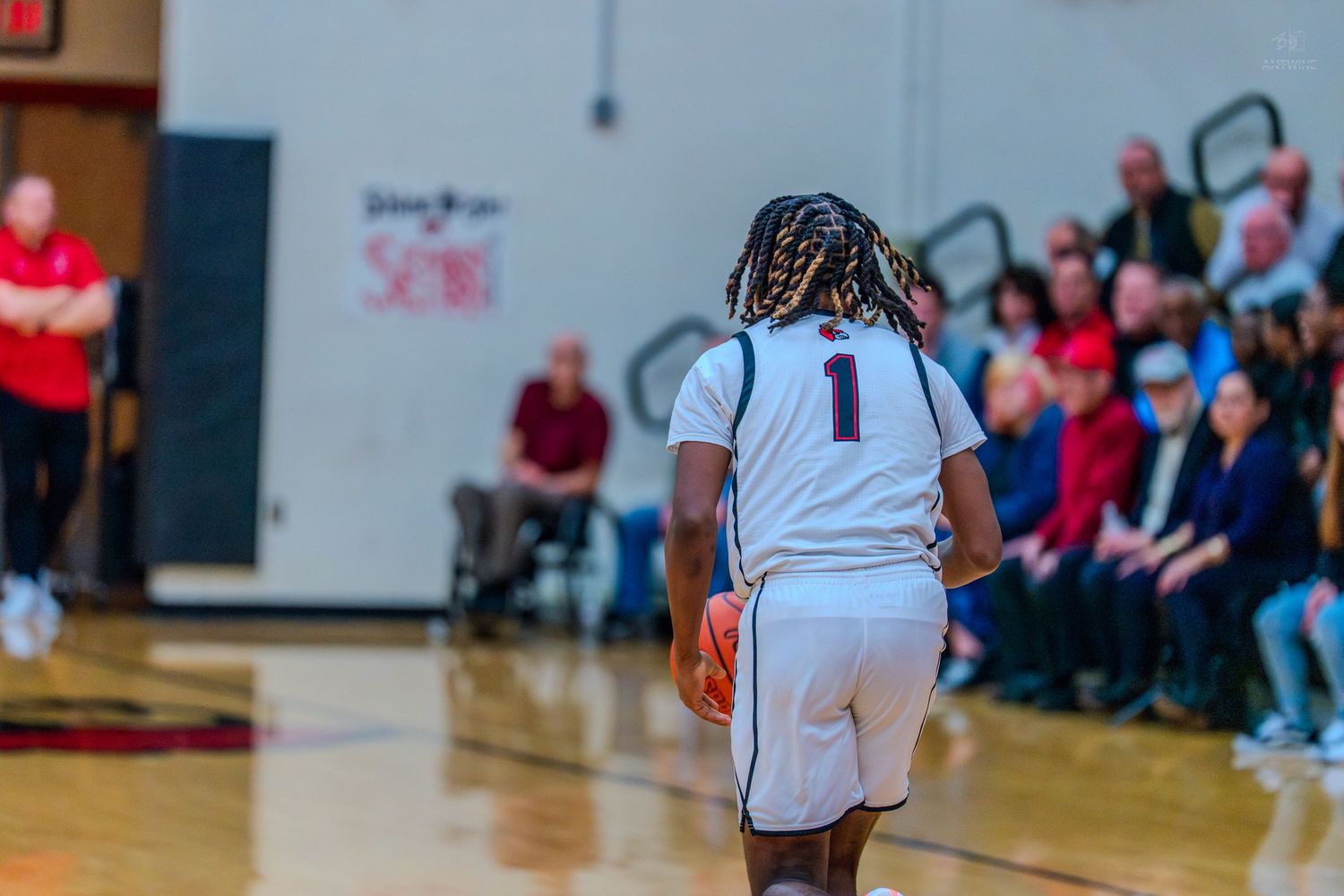High school basketball player #1 with braids dribbles the ball toward the court during a game.