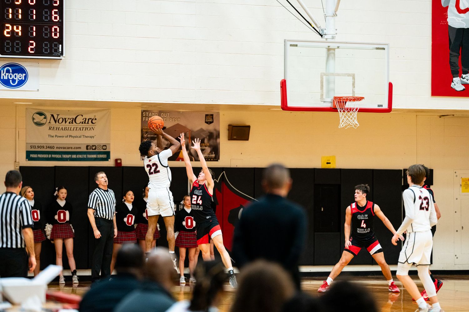 High school basketball player in white shoots over defenders near the basket during indoor gym game.