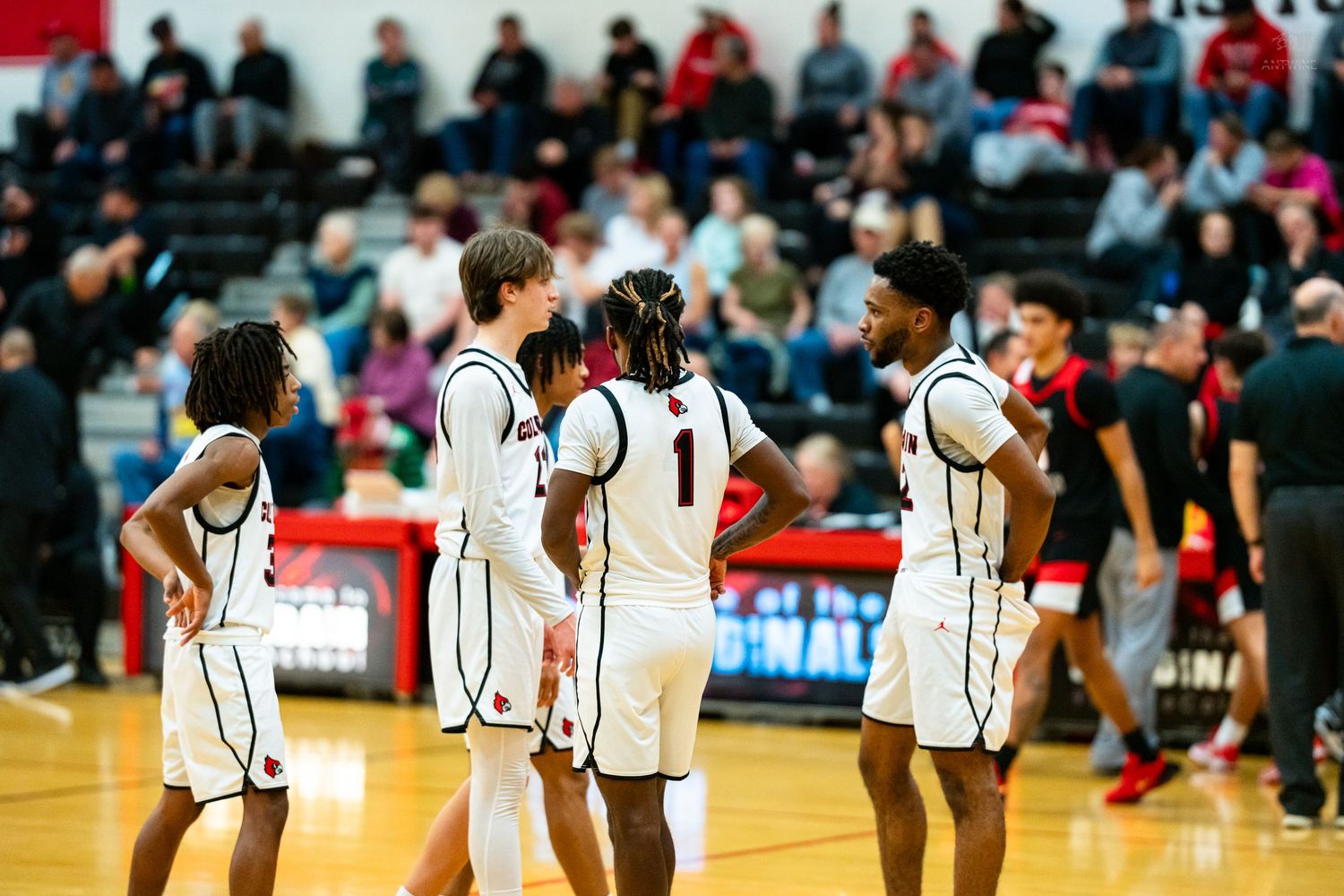 High school basketball players in white uniforms gather on the court during a timeout in a game.