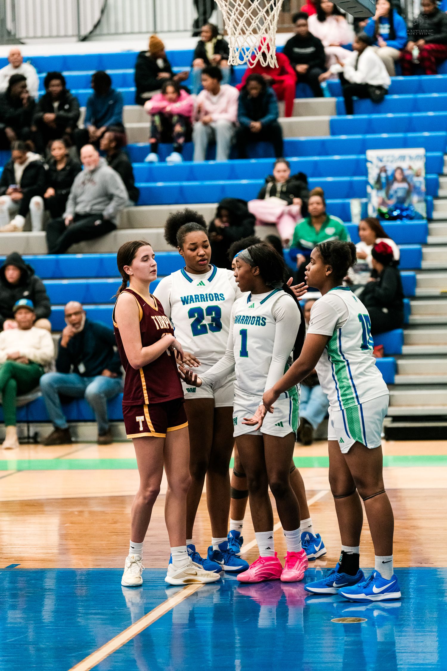 A Turpin player and three Warriors players in white and teal huddle near the basket during a basketball game.