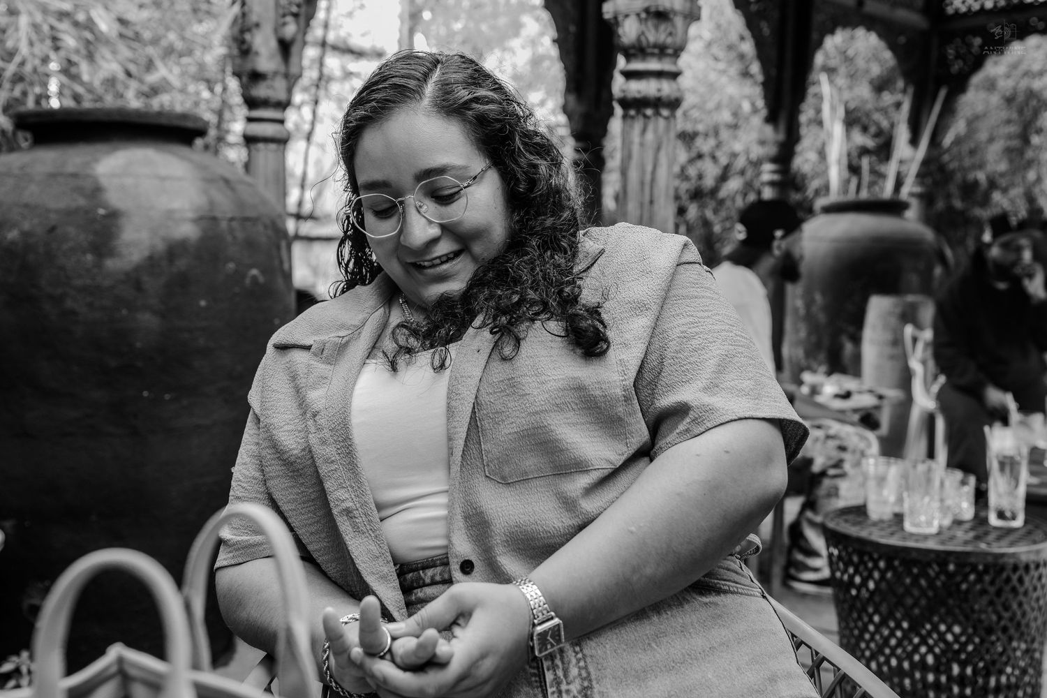 Black and white photo of curly-haired woman in blazer examining something in her hands outdoors.